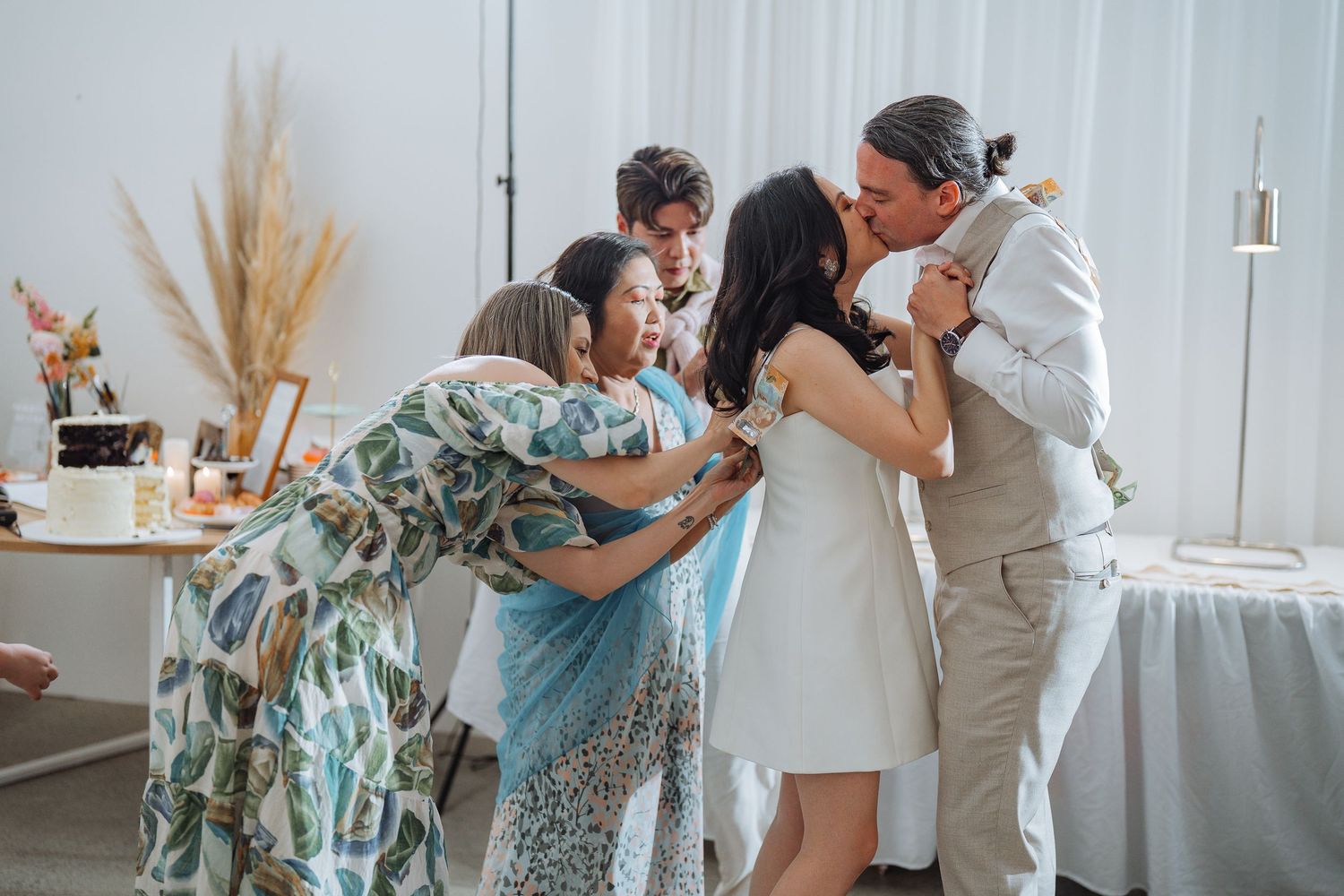 Wedding celebration moment with group embrace in white-decorated indoor setting.