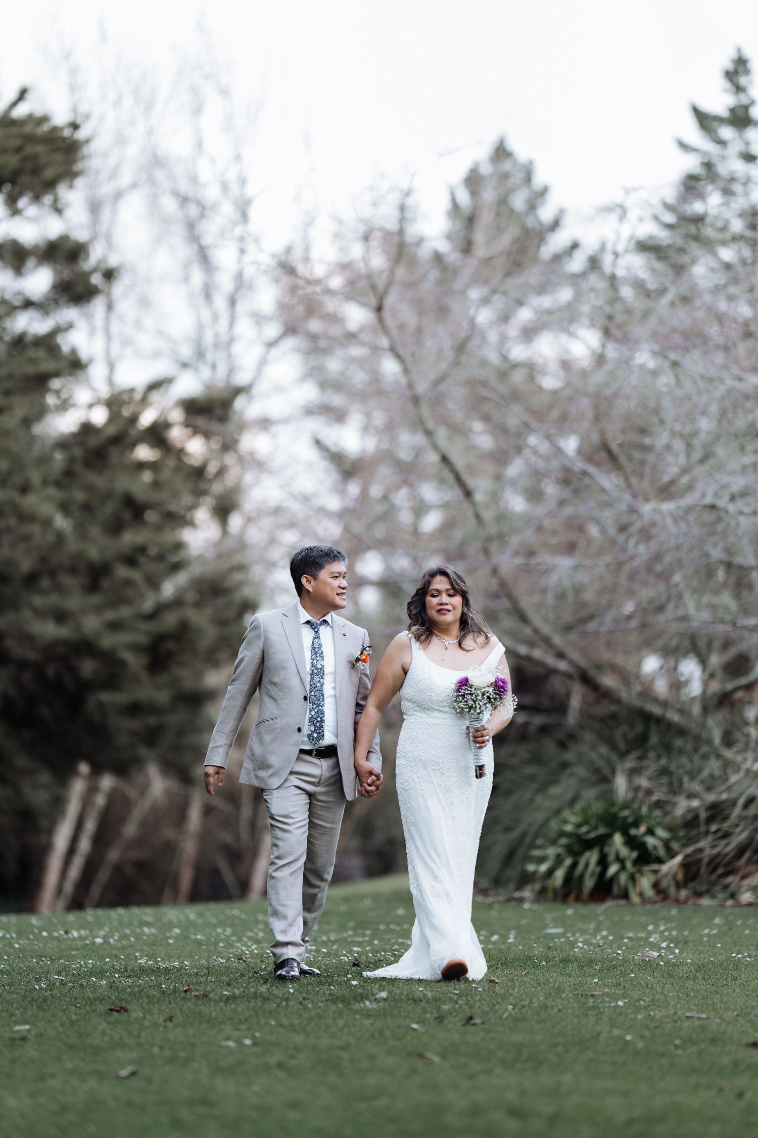 Couple walking hand in hand through garden with blooming trees in romantic outdoor setting.