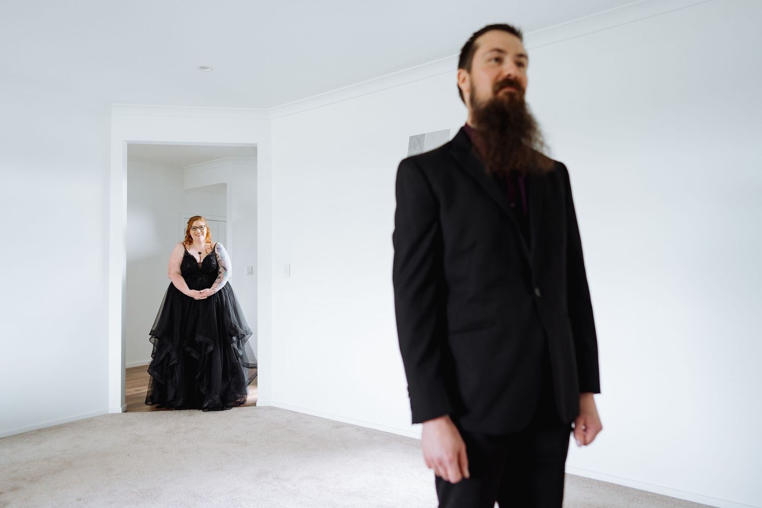 People in formal black attire stand against a stark white interior wall.