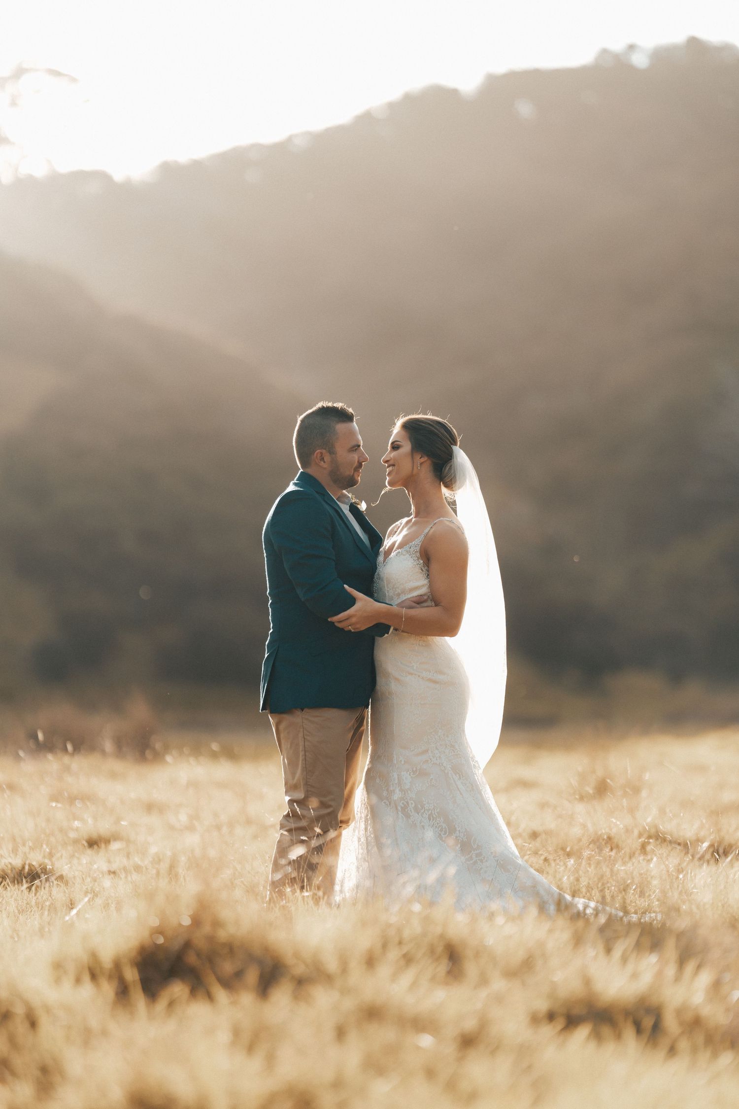 Golden hour wedding portrait in field with mountains and dramatic lighting.