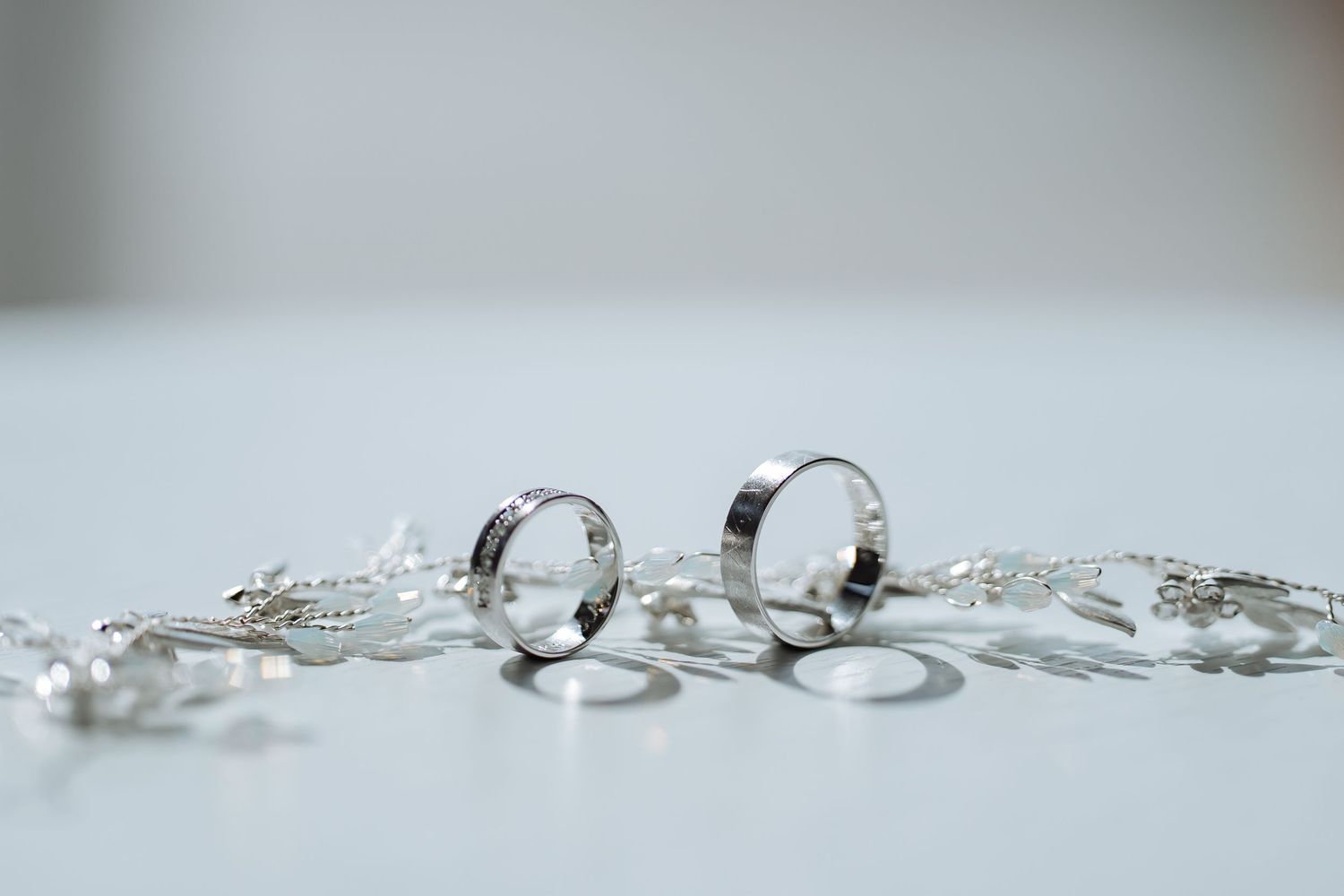 Wedding rings and jewelry arranged artistically on a light gray background.