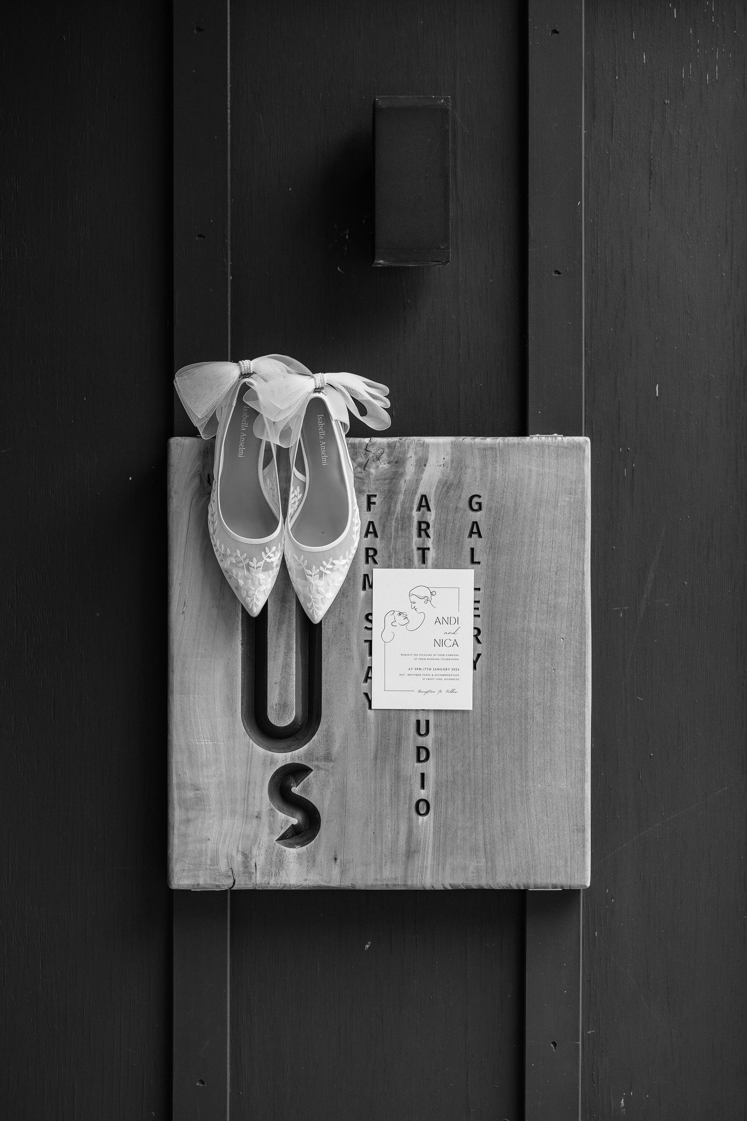 Black and white composition of bridal shoes and wedding stationery on wooden surface.