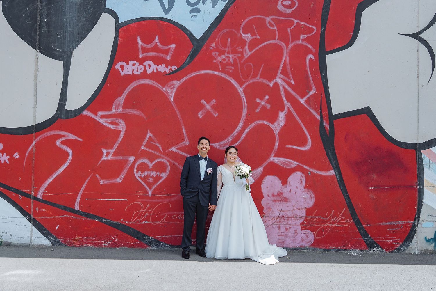 Wedding portrait against vibrant red graffiti wall with urban art.