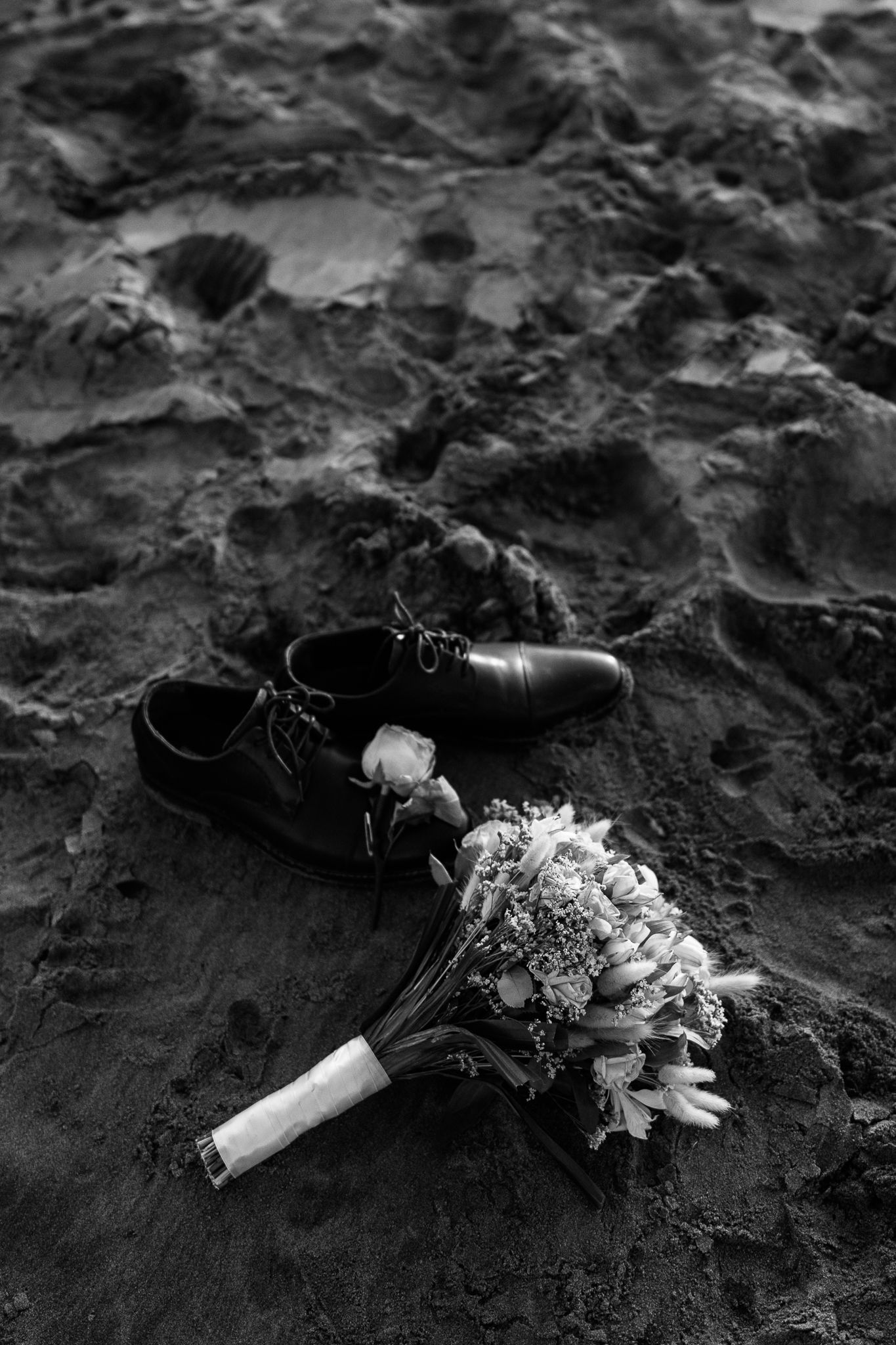 Black and white image of flowers and shoes on textured rocky surface.