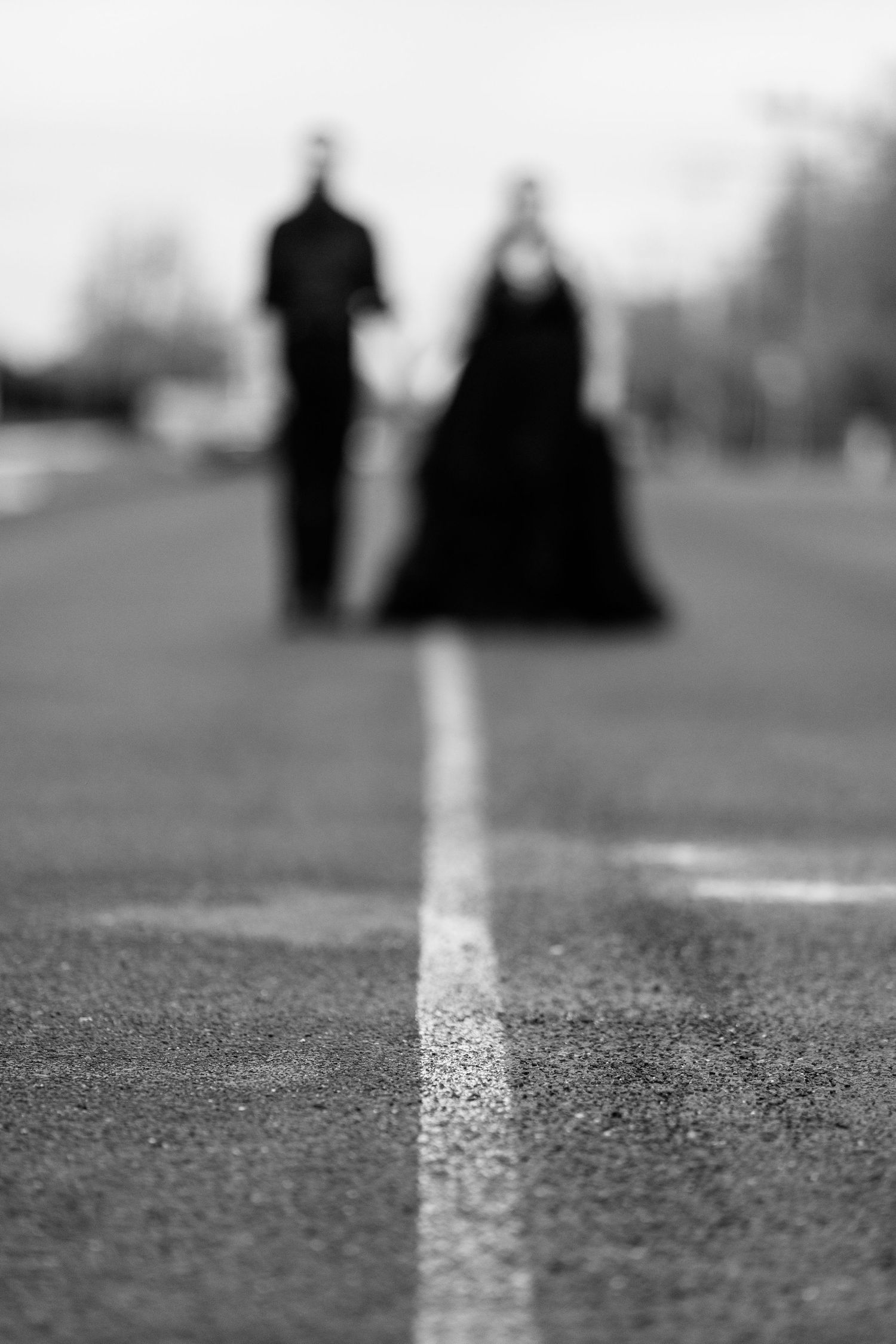 Black and white minimalist photo of a road marking with blurred figures in background.