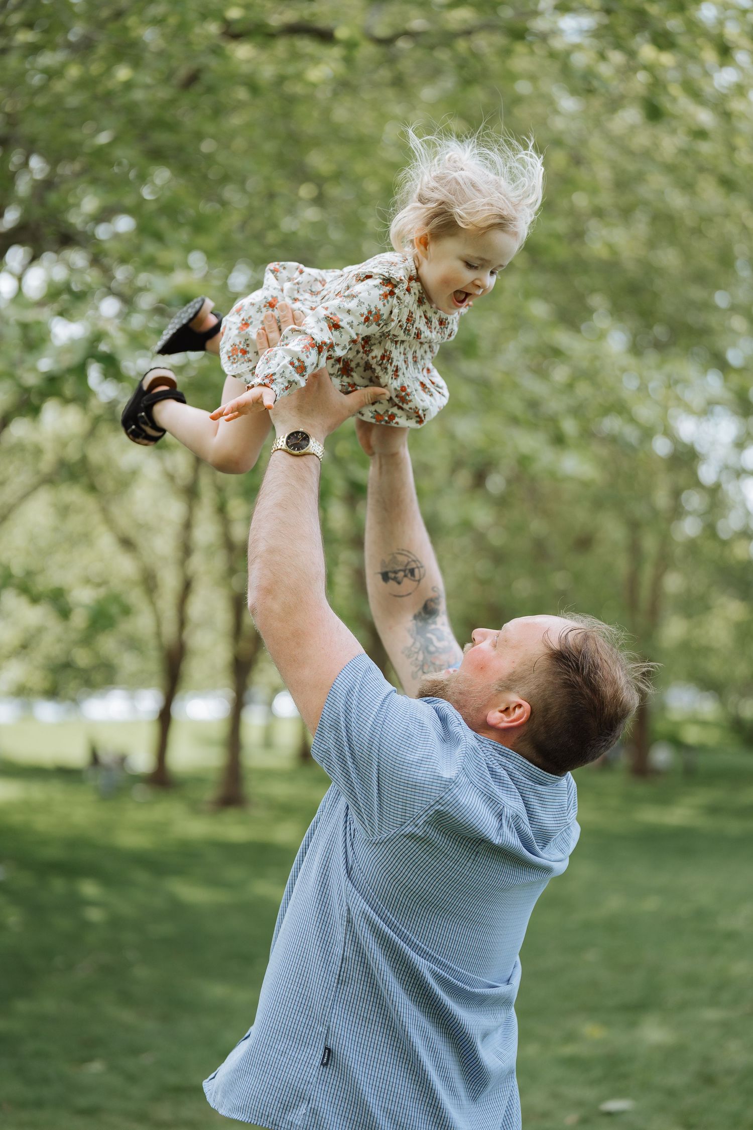 A playful moment as a child is lifted high into the air in a park setting.