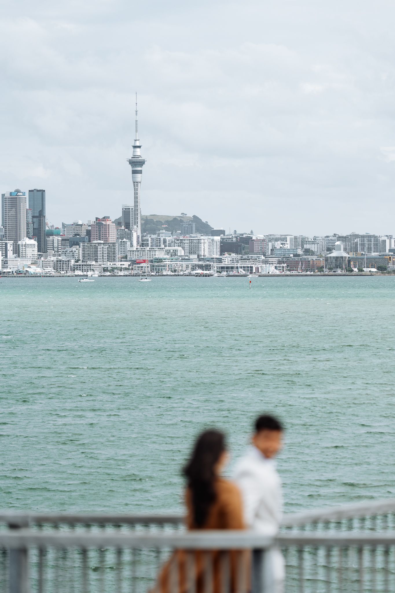 Auckland skyline with Sky Tower visible across the harbor on an overcast day.