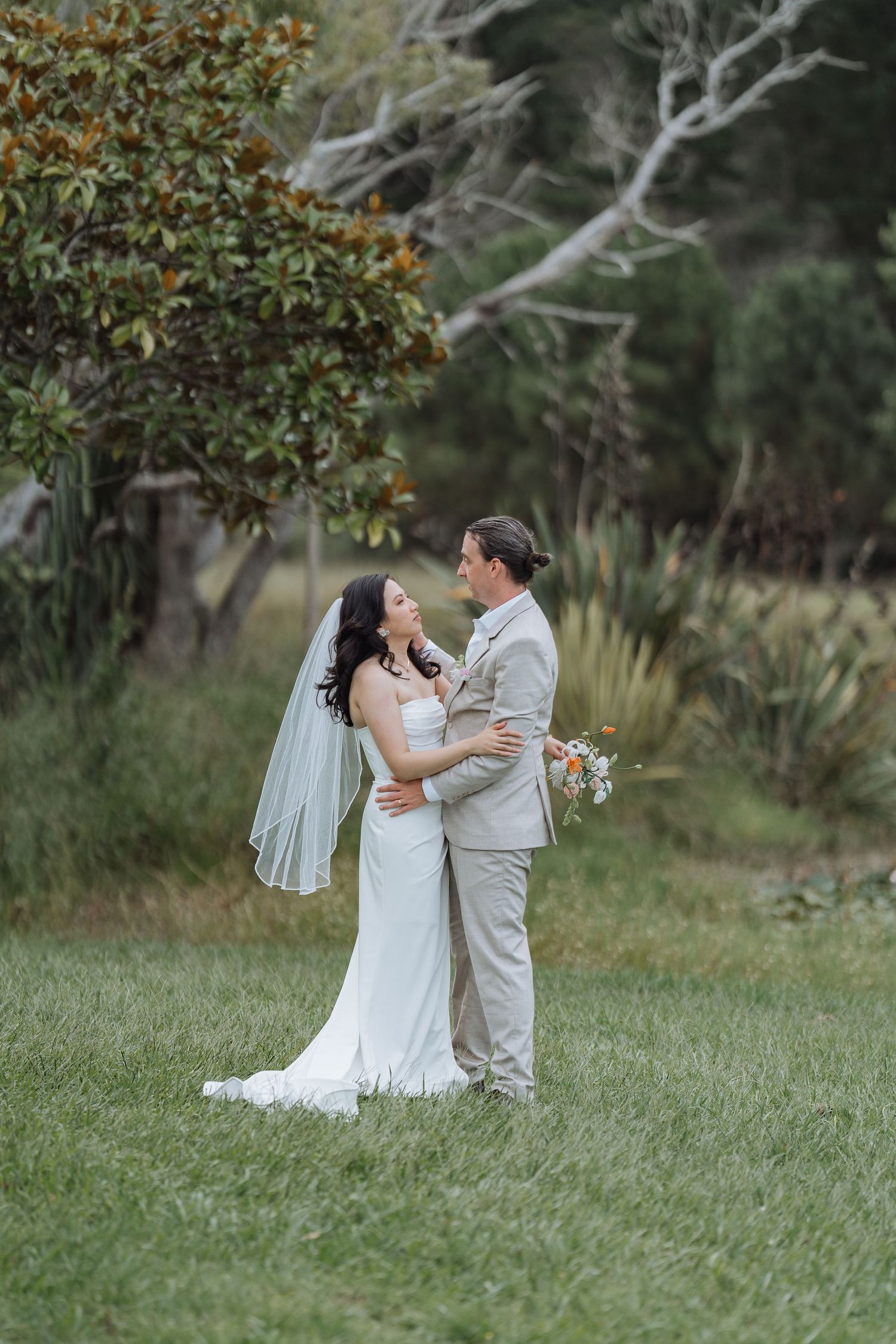 Couple embraces in garden setting with natural foliage backdrop during wedding photoshoot.