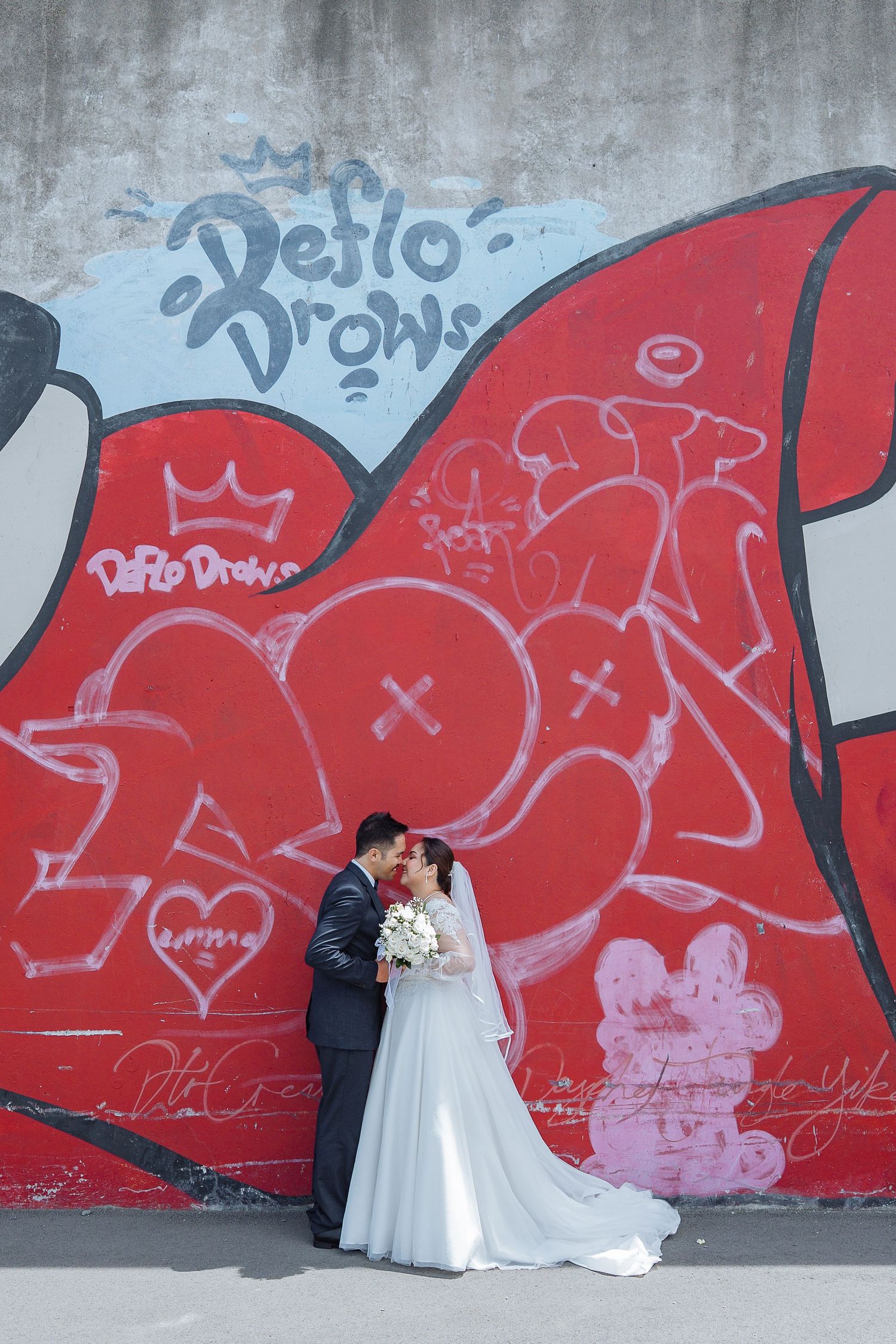 A wedding couple poses against a vibrant red graffiti wall for artistic photos.