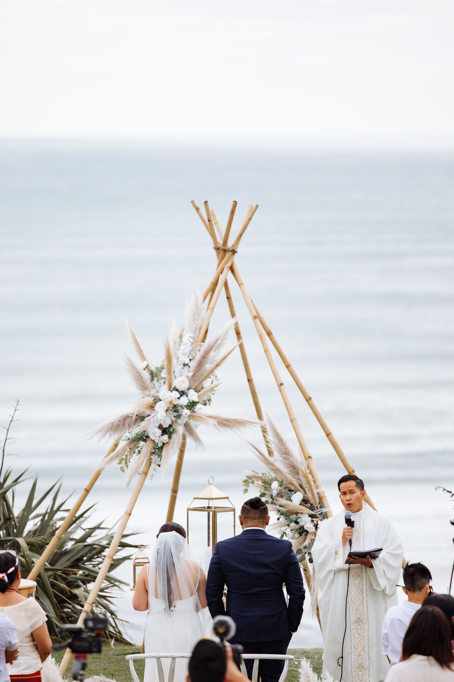 Beach wedding ceremony setup with wooden teepees decorated with tropical flowers.