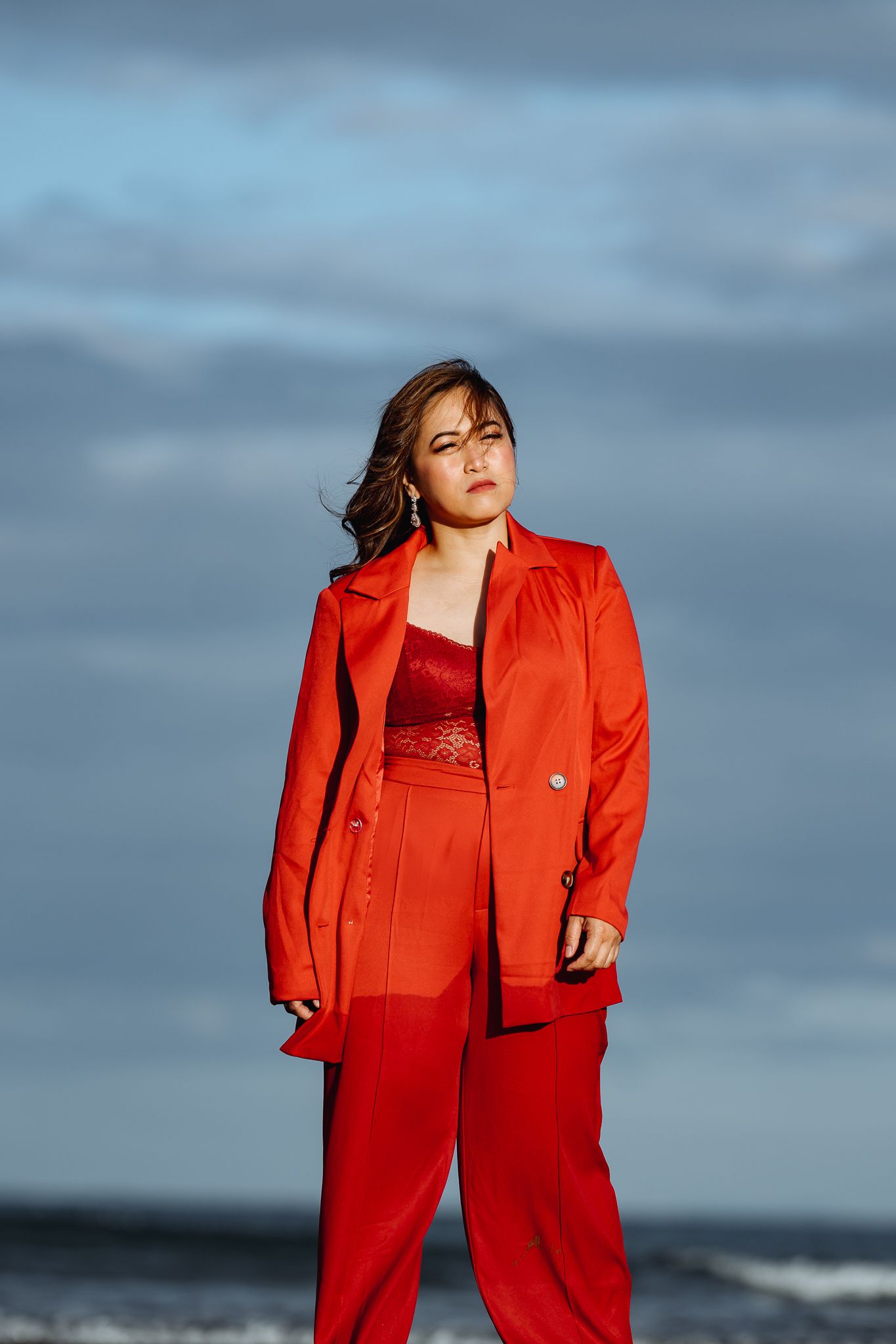 A person in a striking red pantsuit stands confidently against a moody seaside backdrop.