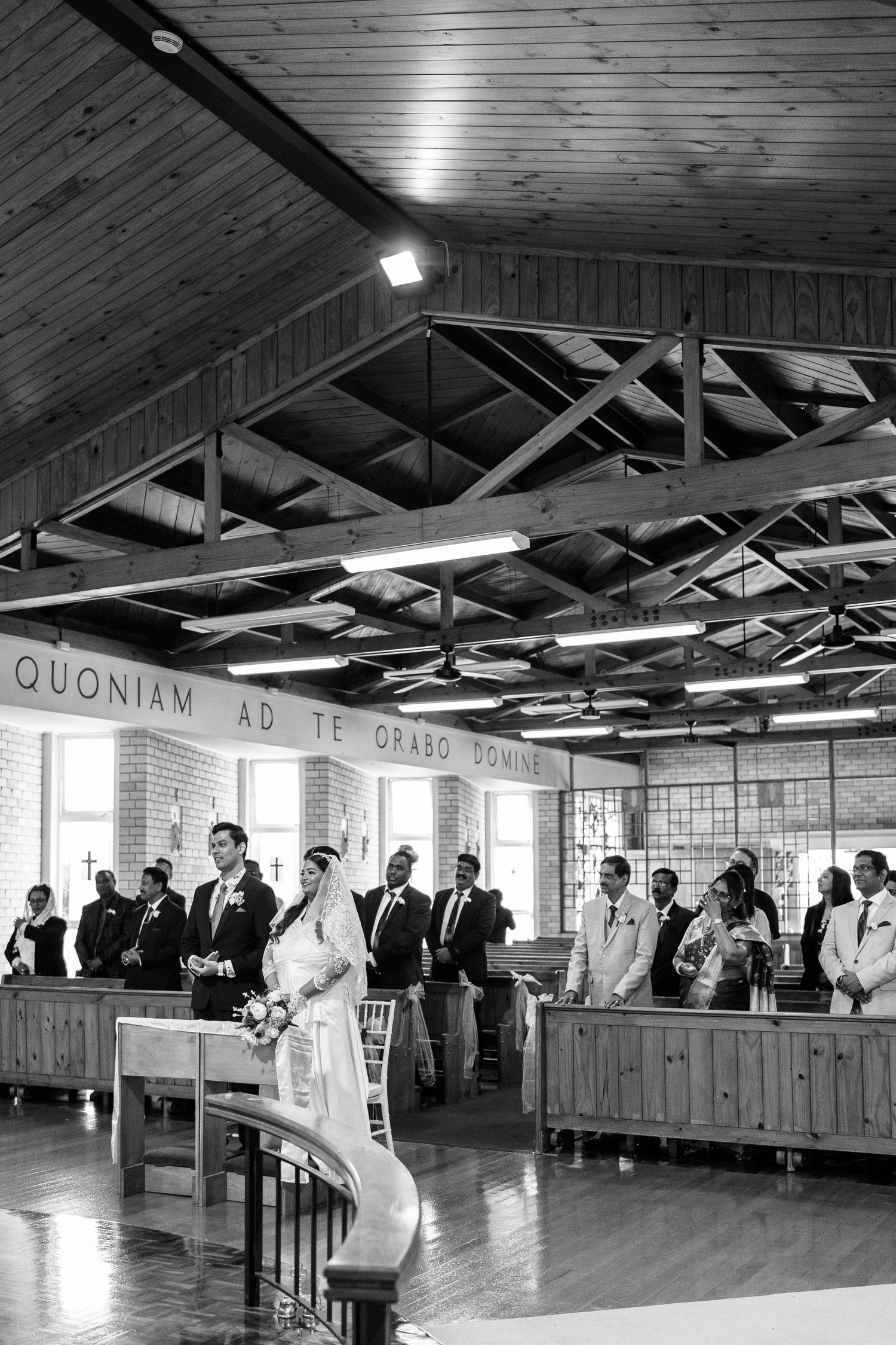 A panoramic view of a rustic indoor wedding venue with wooden ceiling beams and guests seated.