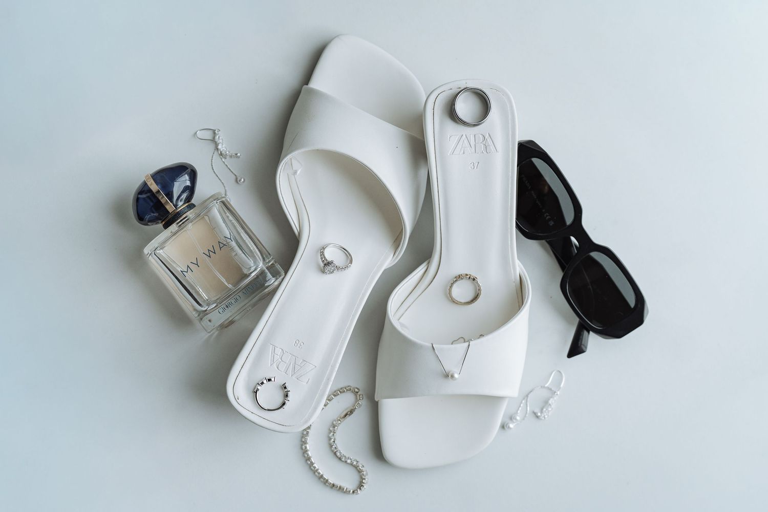 Wedding accessories including rings and jewelry arranged artistically on white background.