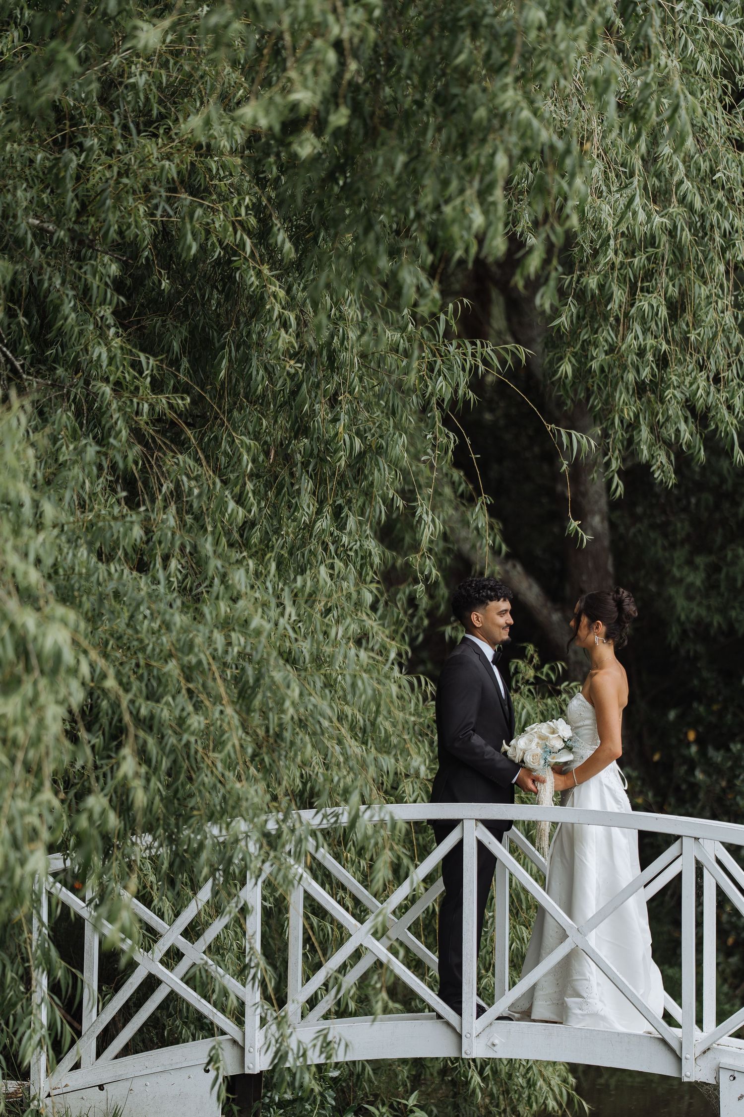 Romantic moment captured on a white wooden bridge surrounded by willow trees.