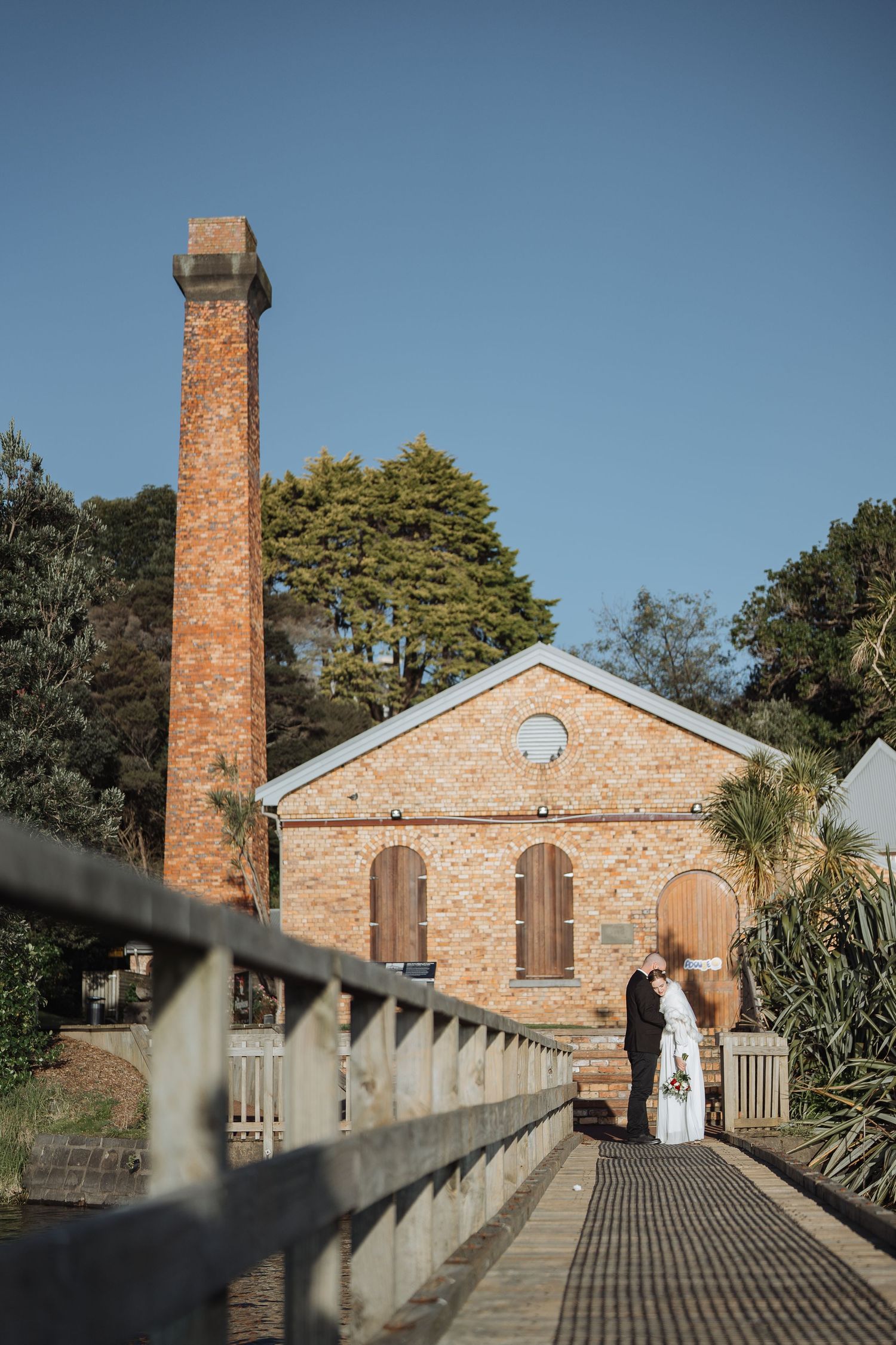 Historic brick church with tall chimney and walkway under bright blue sky.