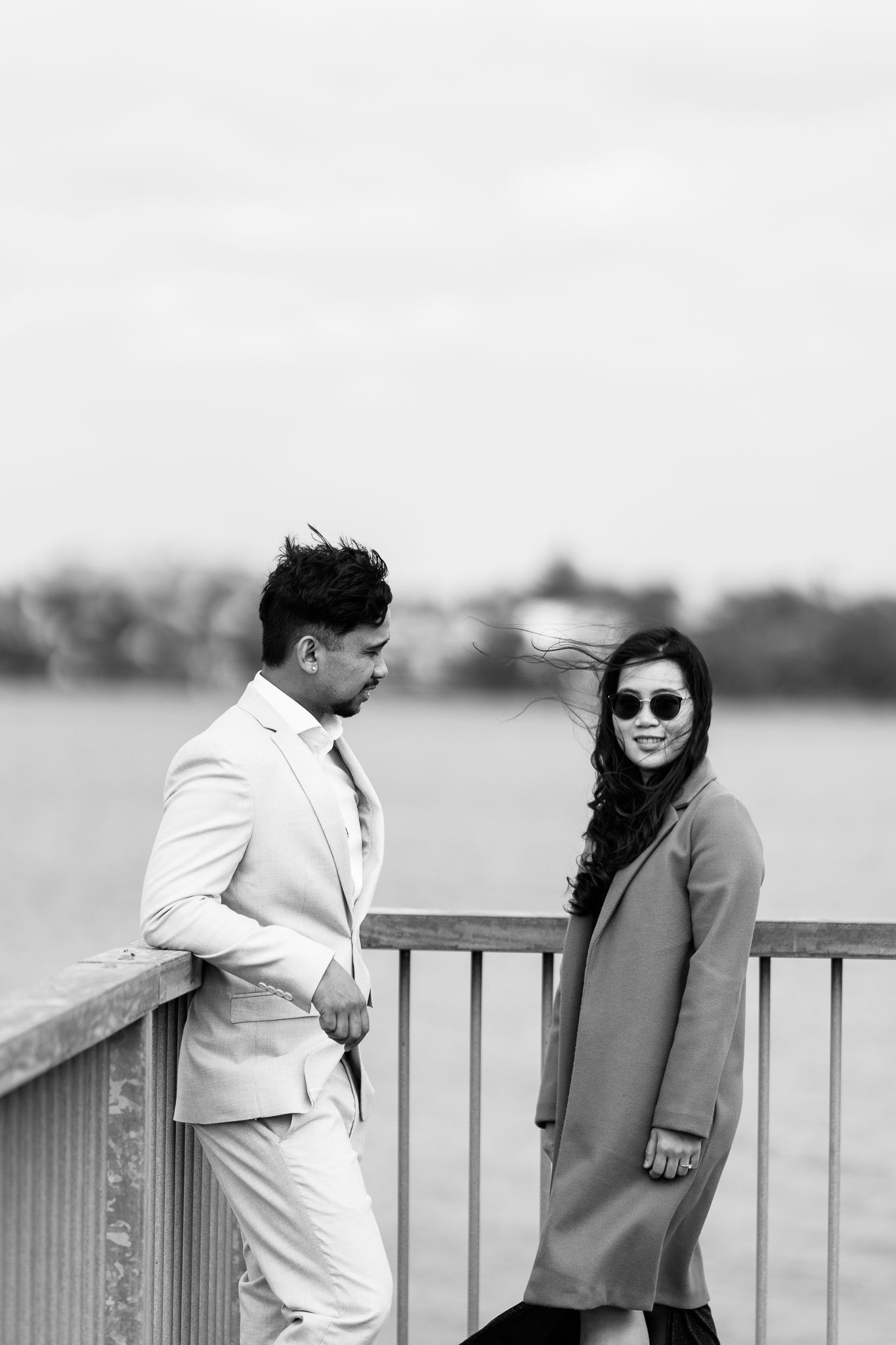 Couple poses together on a waterfront boardwalk with city skyline in background.