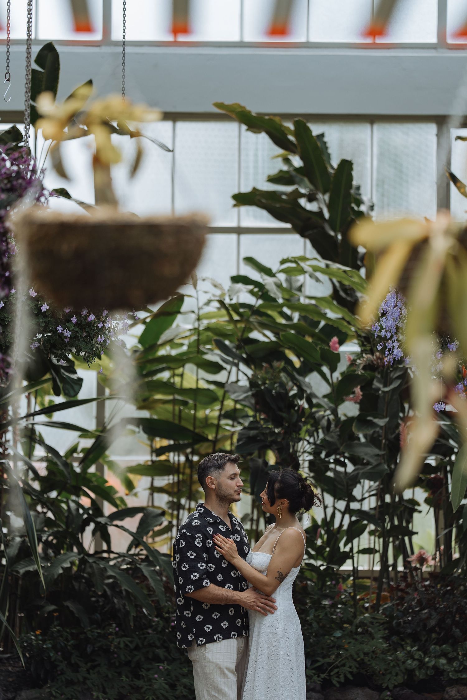 Couple sharing an intimate moment in a greenhouse surrounded by lush plants.