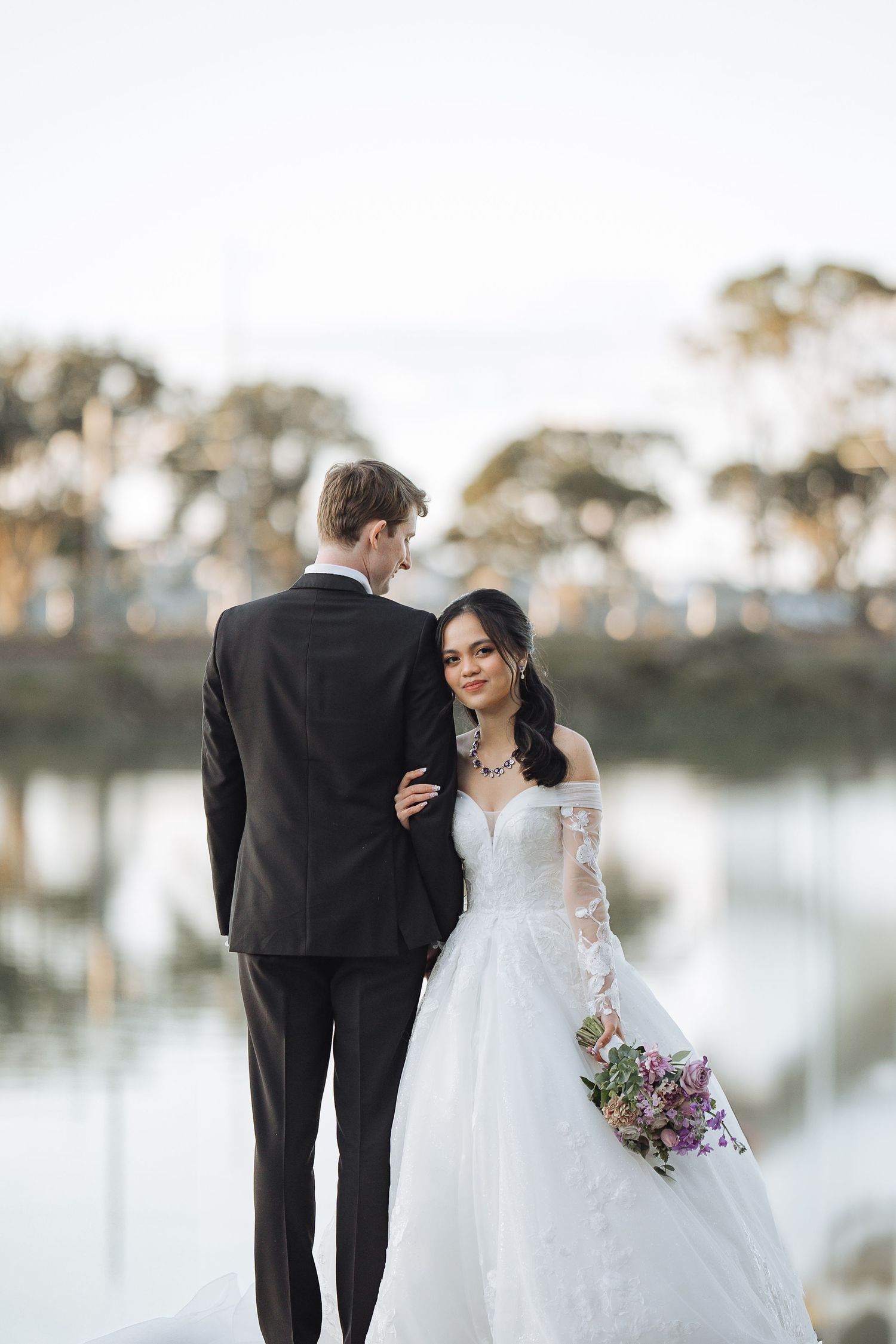 Romantic wedding couple poses by a serene lake during golden hour.