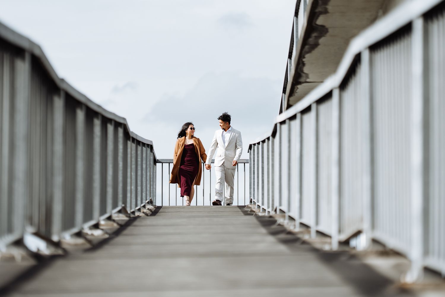 Two people stand at the end of a long white bridge walkway.