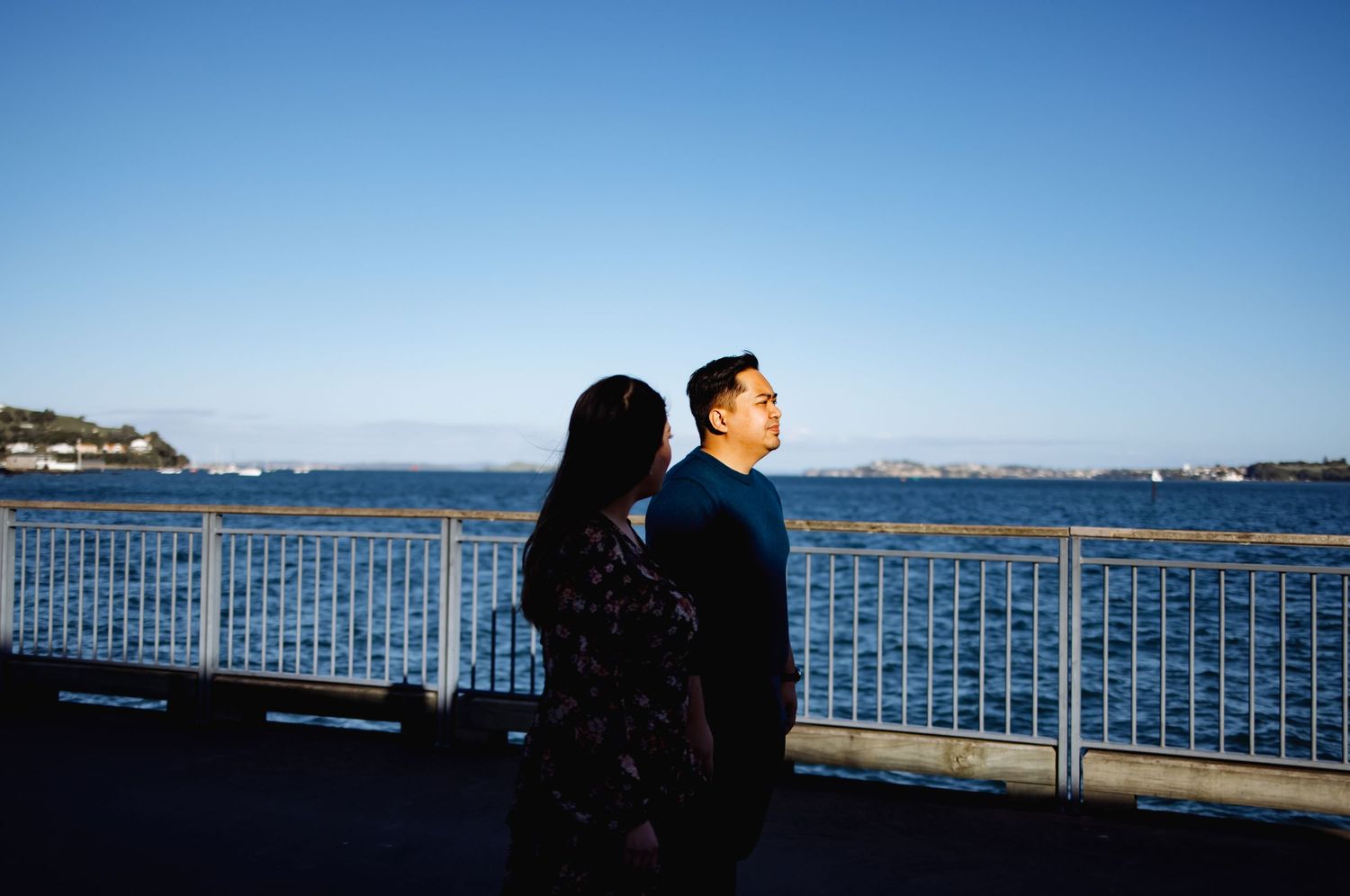 Two figures in silhouette against a bright ocean backdrop with railing.