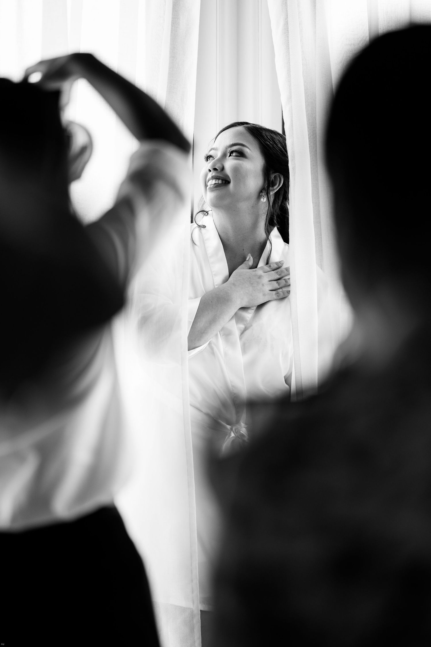 Artistic black and white getting ready moments captured through sheer curtains.