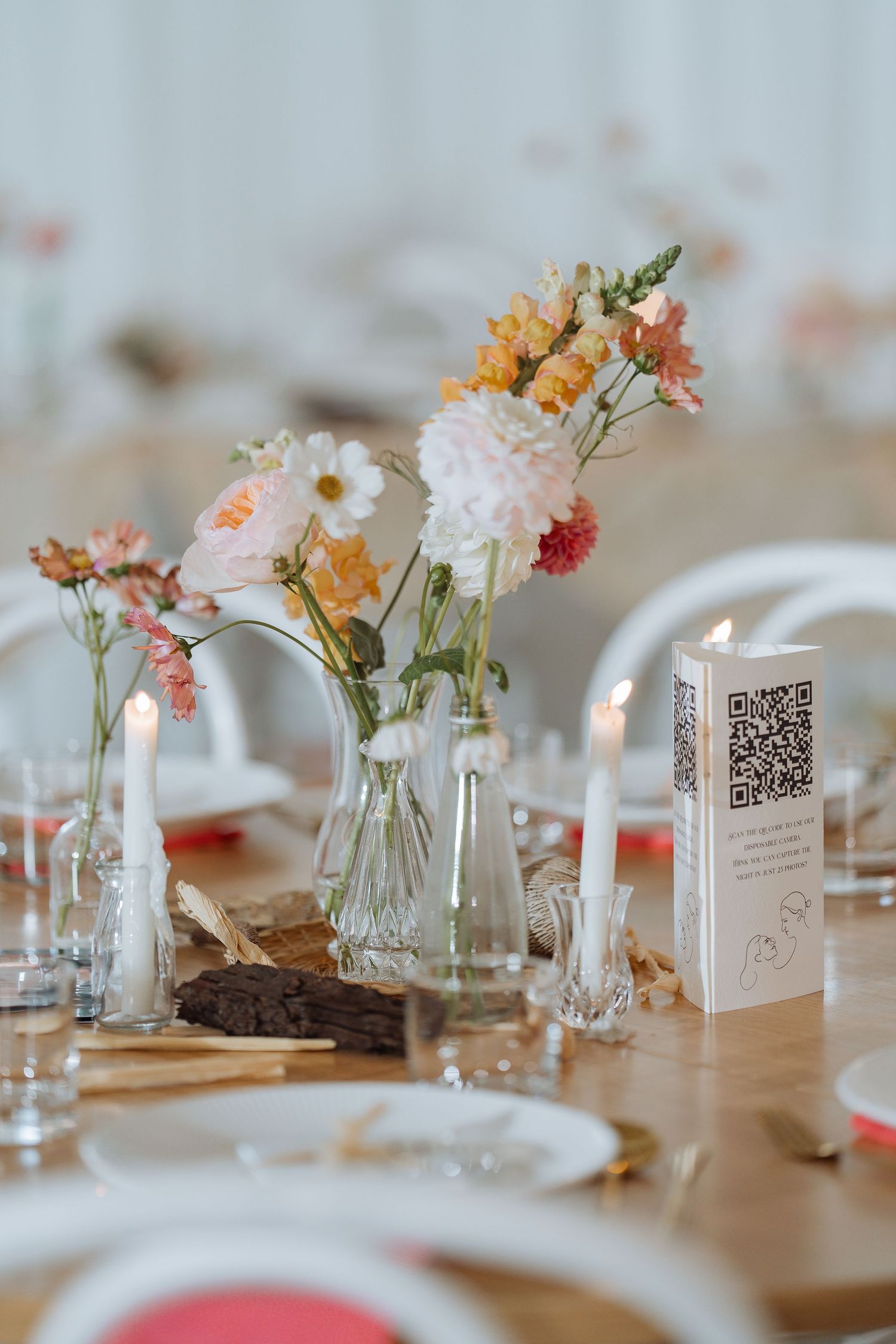 Wedding table setting with delicate floral centerpieces in glass vases and QR code display card.