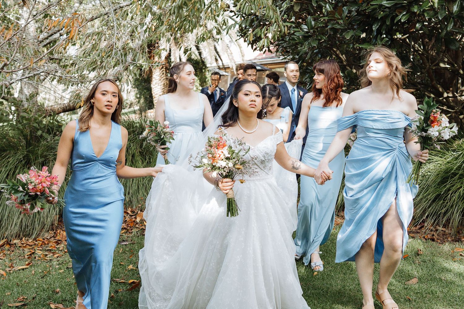 Wedding party poses outdoors wearing light blue bridesmaid dresses alongside the bride in white.