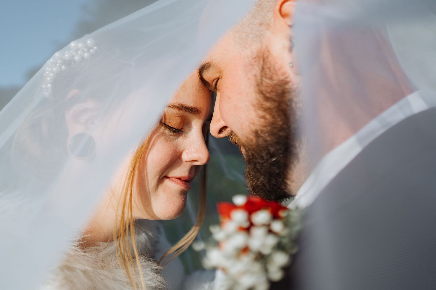 Close-up romantic moment between bride and groom under veil.
