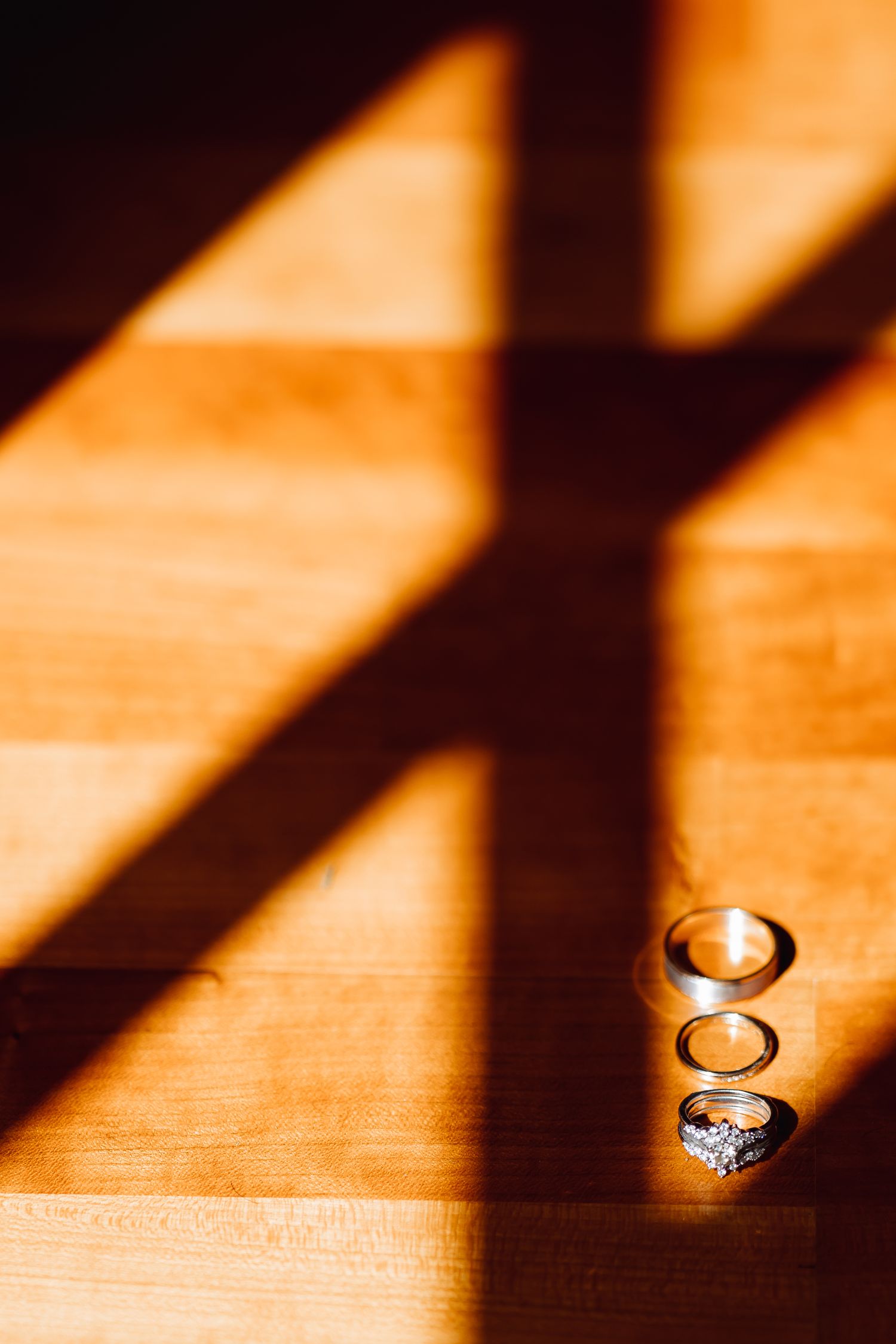 Wedding rings casting dramatic shadows on wooden surface in warm lighting.