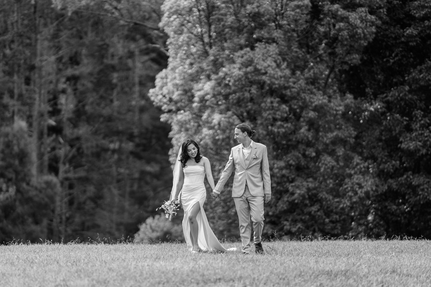 Black and white photo of couple walking hand in hand across hillside during wedding portraits.