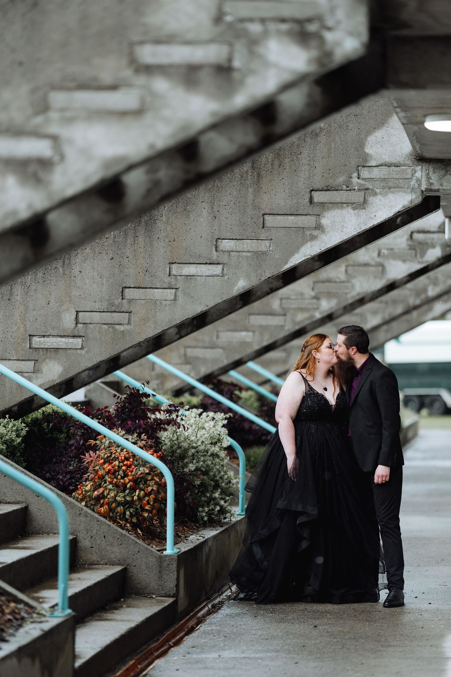 Romantic moment captured under concrete stairs with turquoise railings.