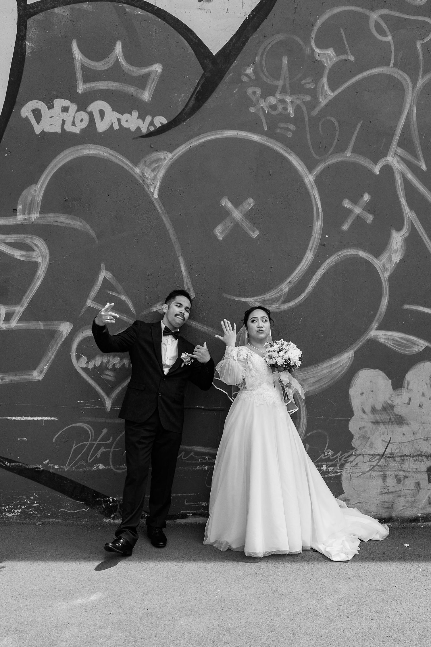 Black and white wedding portrait with couple posing against street art mural.