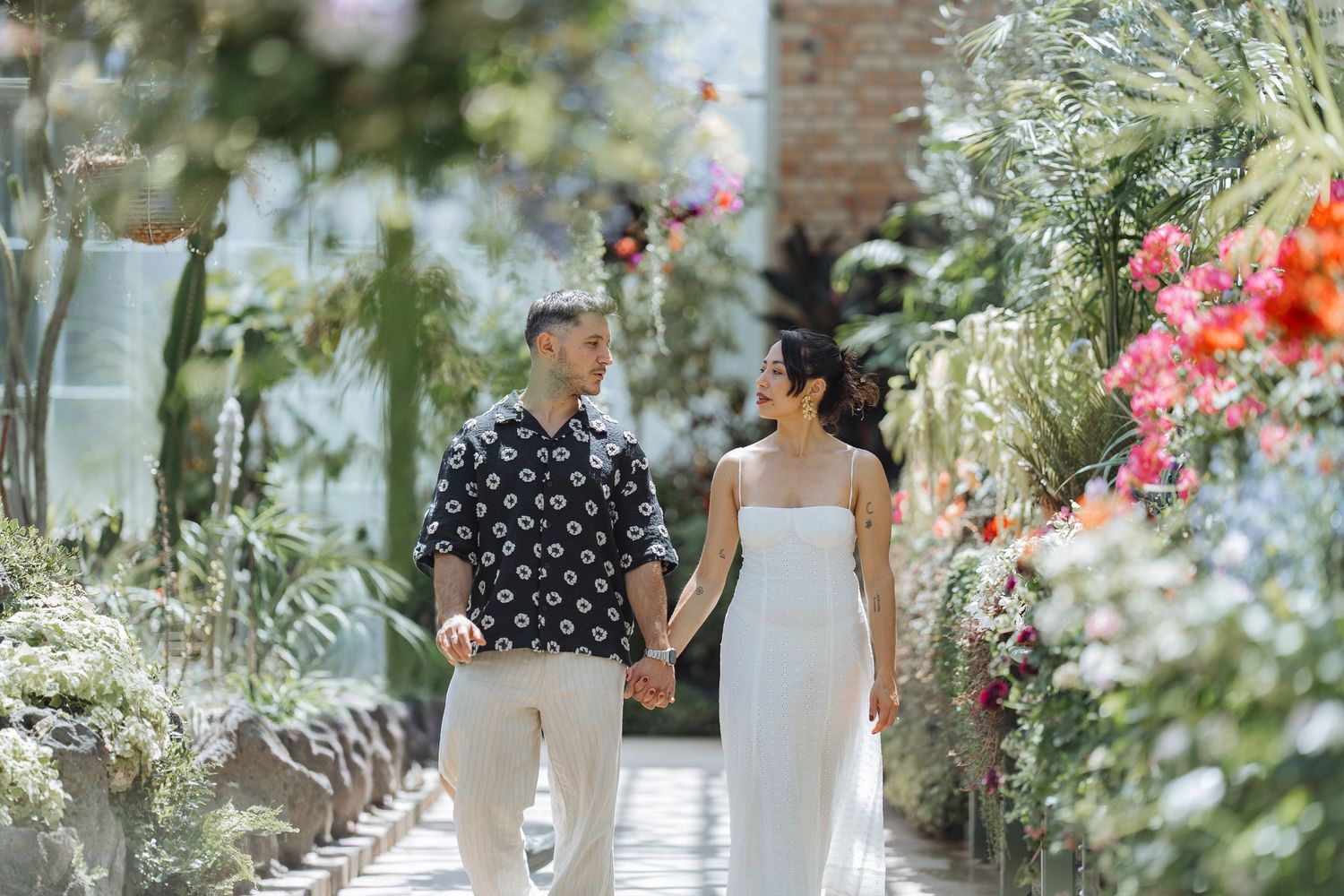 Romantic greenhouse photoshoot with couple surrounded by blooming flowers and greenery.