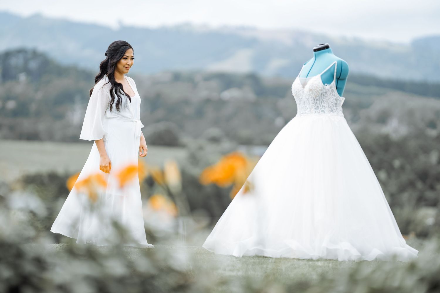 Bride in flowing white dress running through a meadow with mountains in the distance.