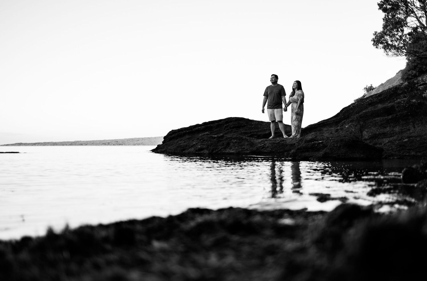Silhouettes of two people walking along a scenic coastline at sunset.