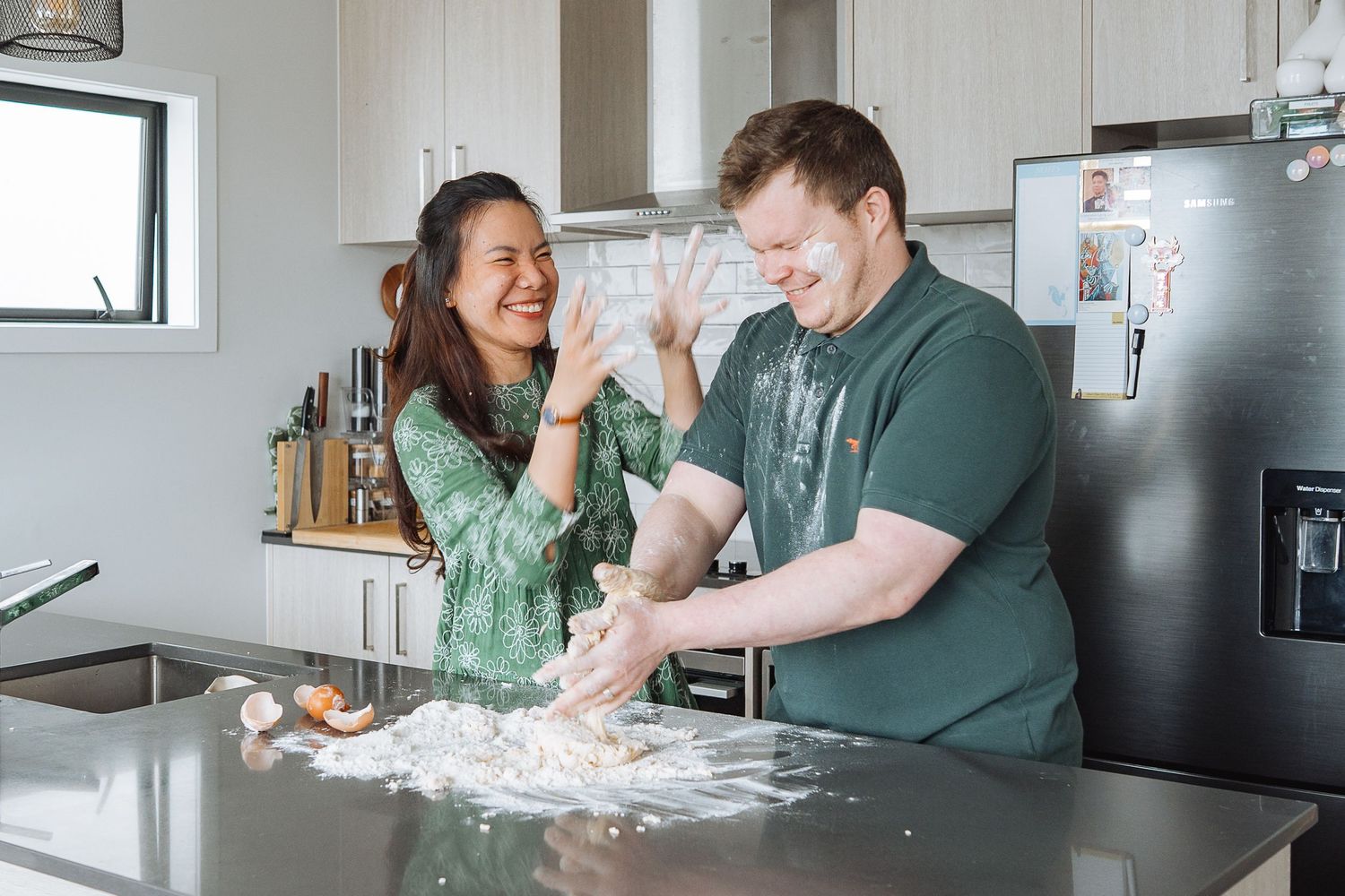 A couple laughs while baking together in a modern kitchen.