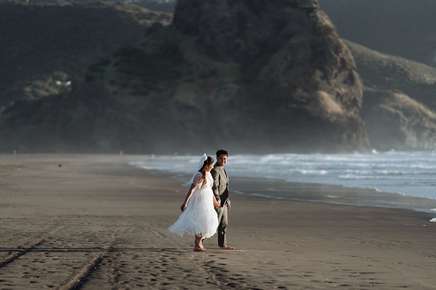 Couple walking along scenic beach with cliffs and ocean waves in background.