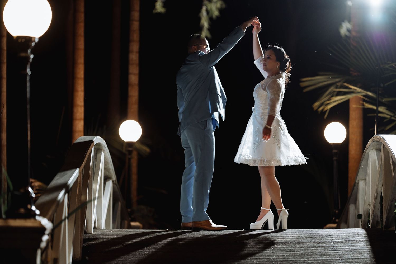 Couple dancing on bridge at night with romantic lighting and glowing lanterns.