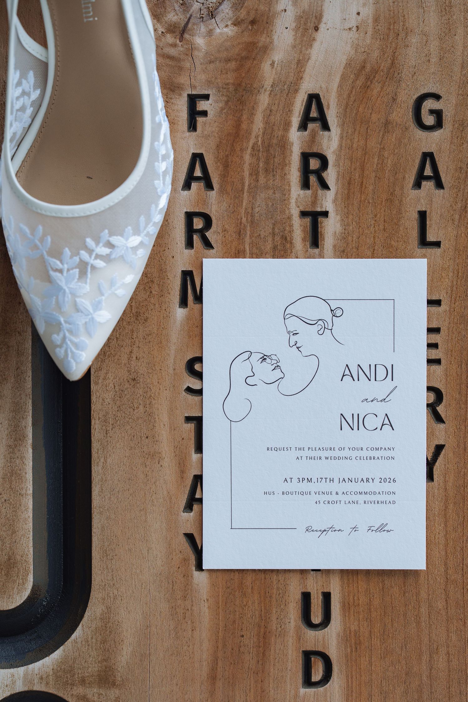 Elegant white bridal shoes and wedding invitation arranged on rustic wooden background.