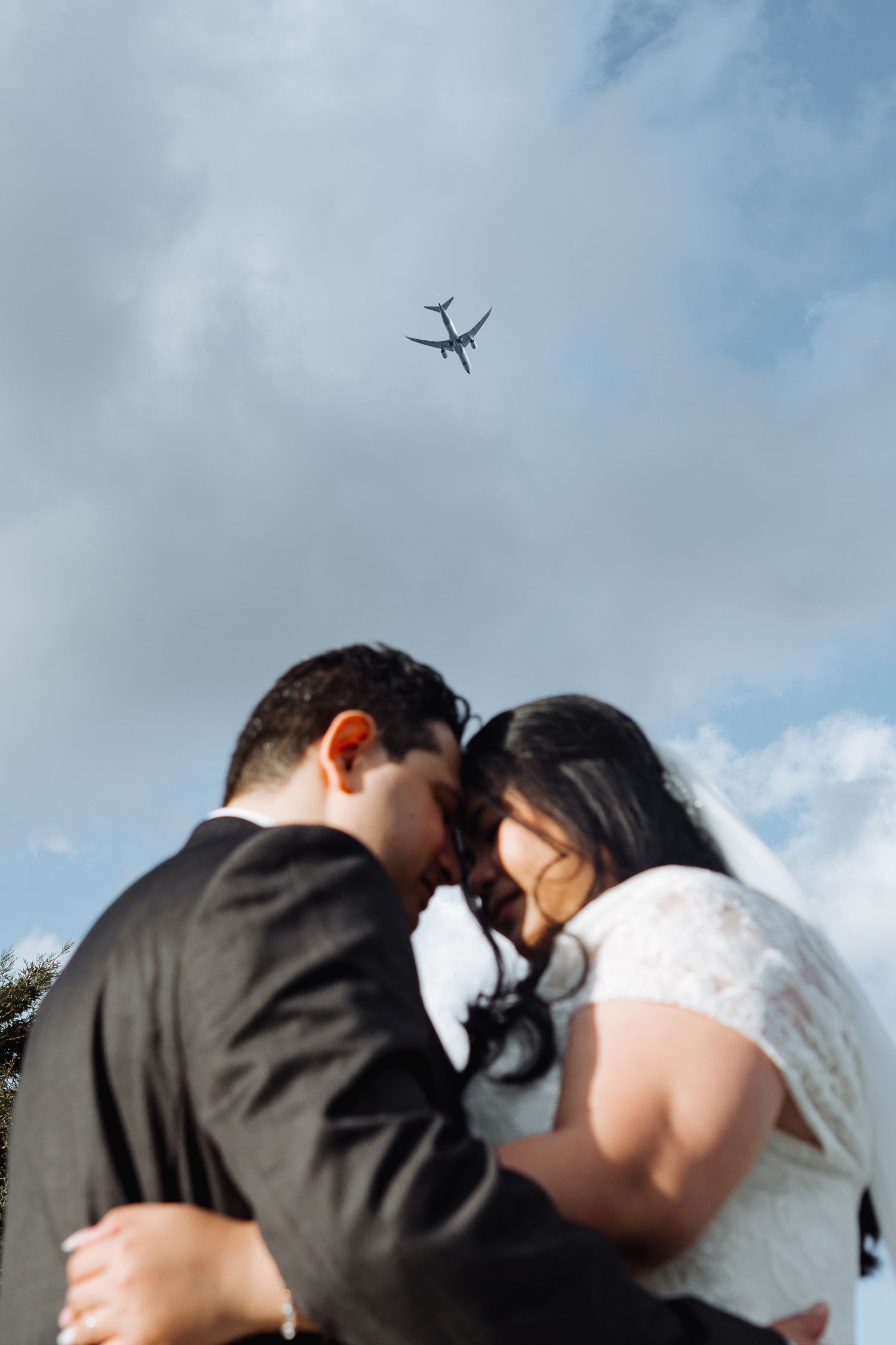 Romantic couple embraces under blue sky with clouds during outdoor wedding photoshoot.