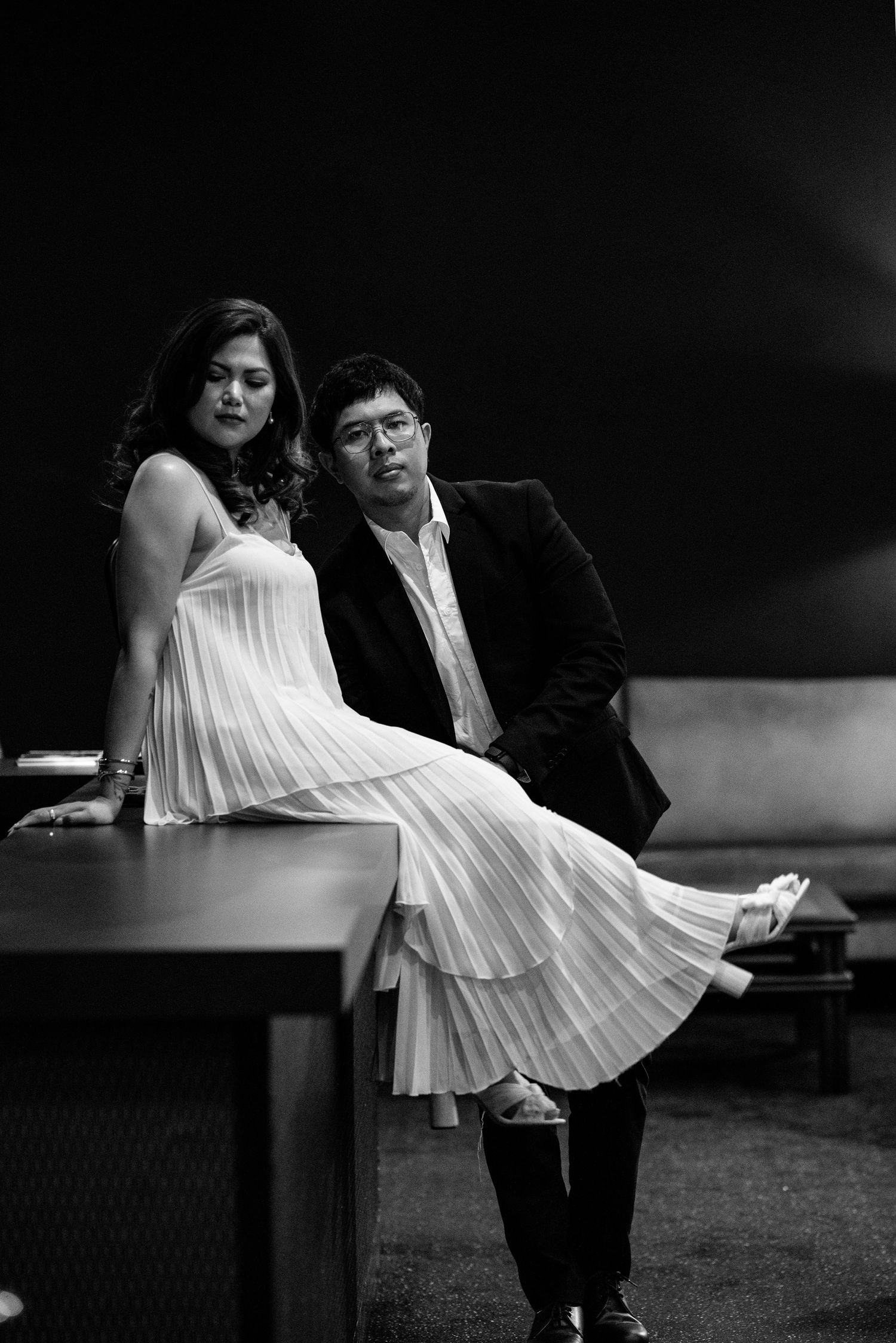 Artistic black and white photo of a couple with woman in pleated white dress.