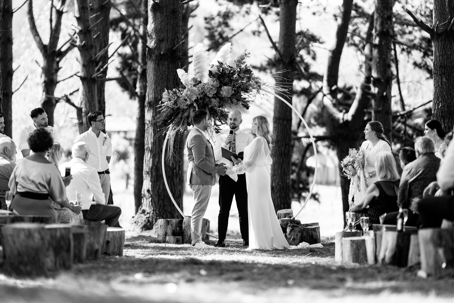 A black and white panorama of wedding guests gathered at an outdoor ceremony venue.