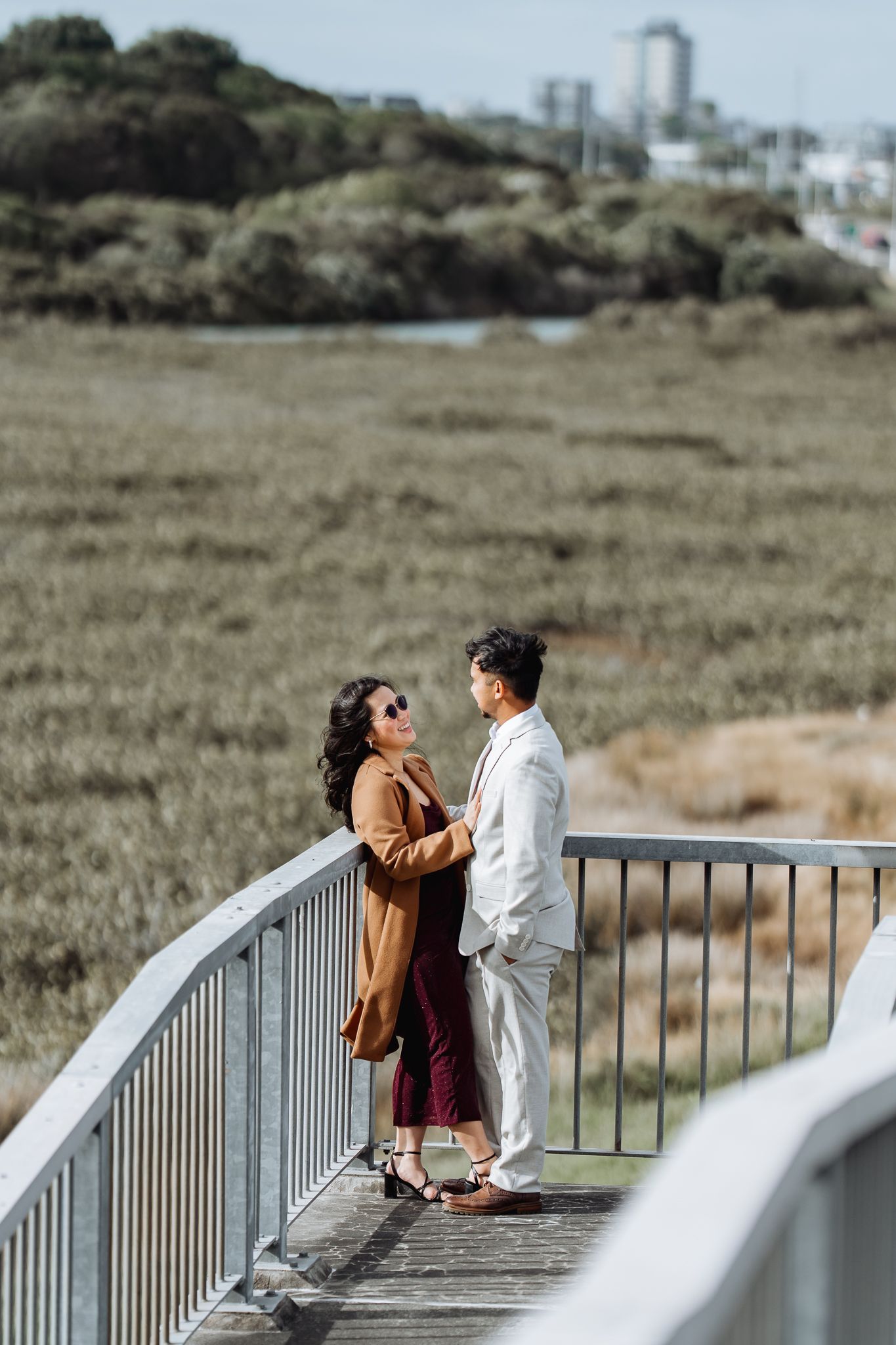 Couple sharing a moment together on a railed walkway overlooking a grassy coastal landscape.