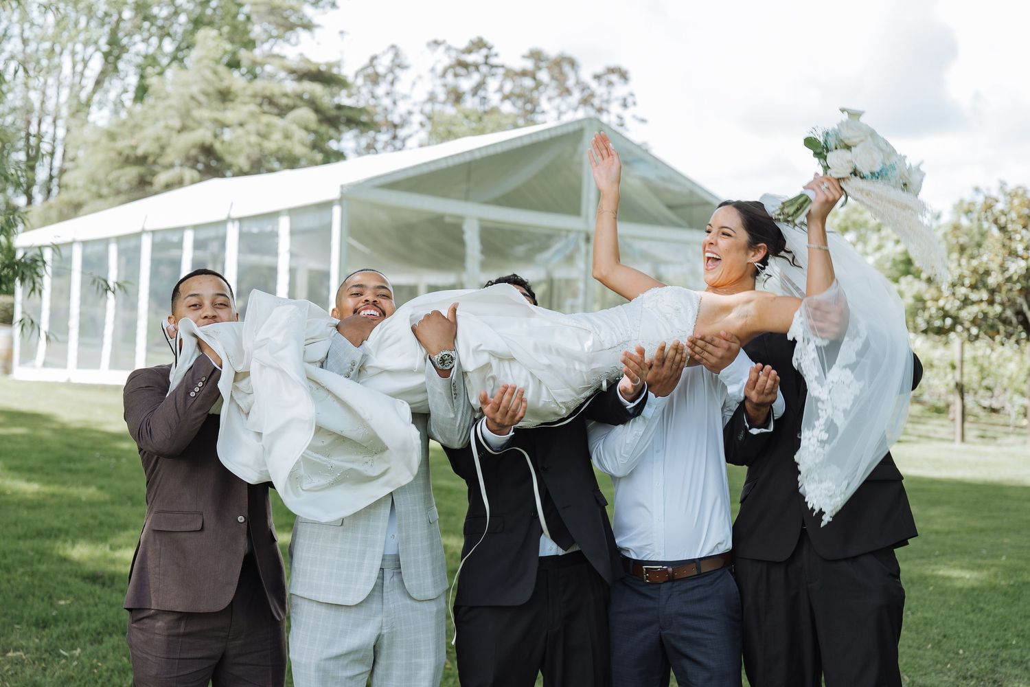 Groomsmen in formal attire celebrating and having fun outdoors.
