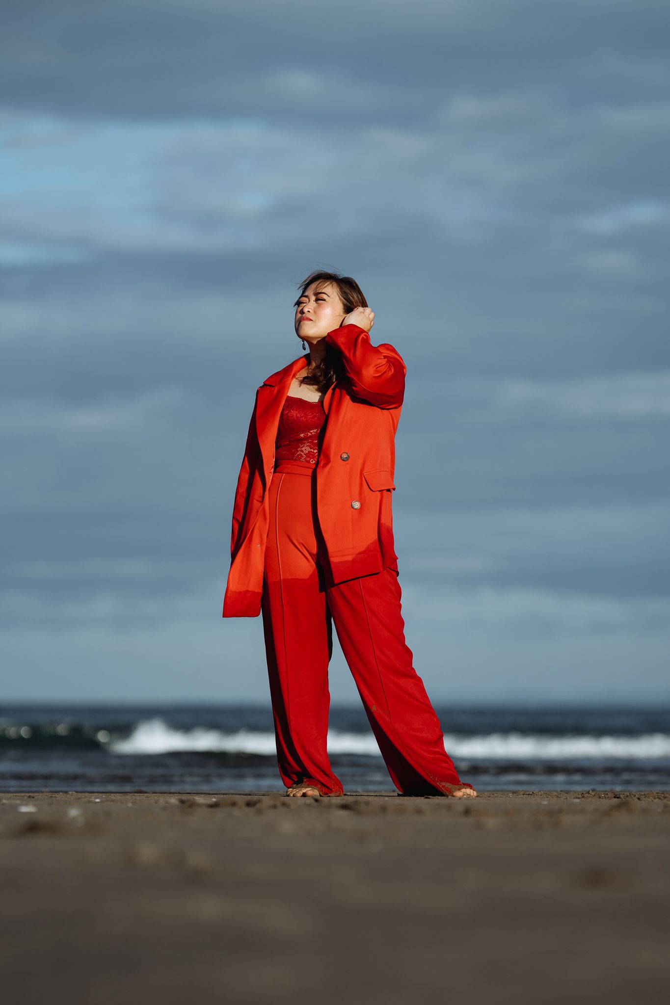 Person in red jumpsuit performs dynamic movements against dramatic coastal backdrop.