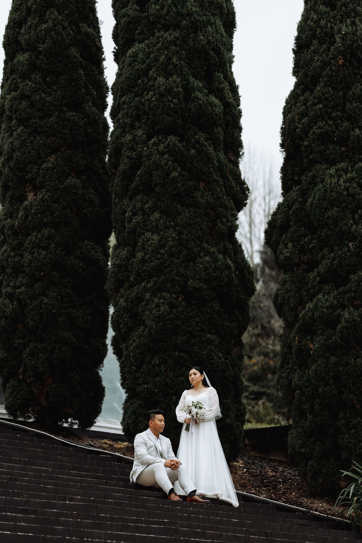 Wedding photo session with tall cypress trees creating dramatic backdrop.