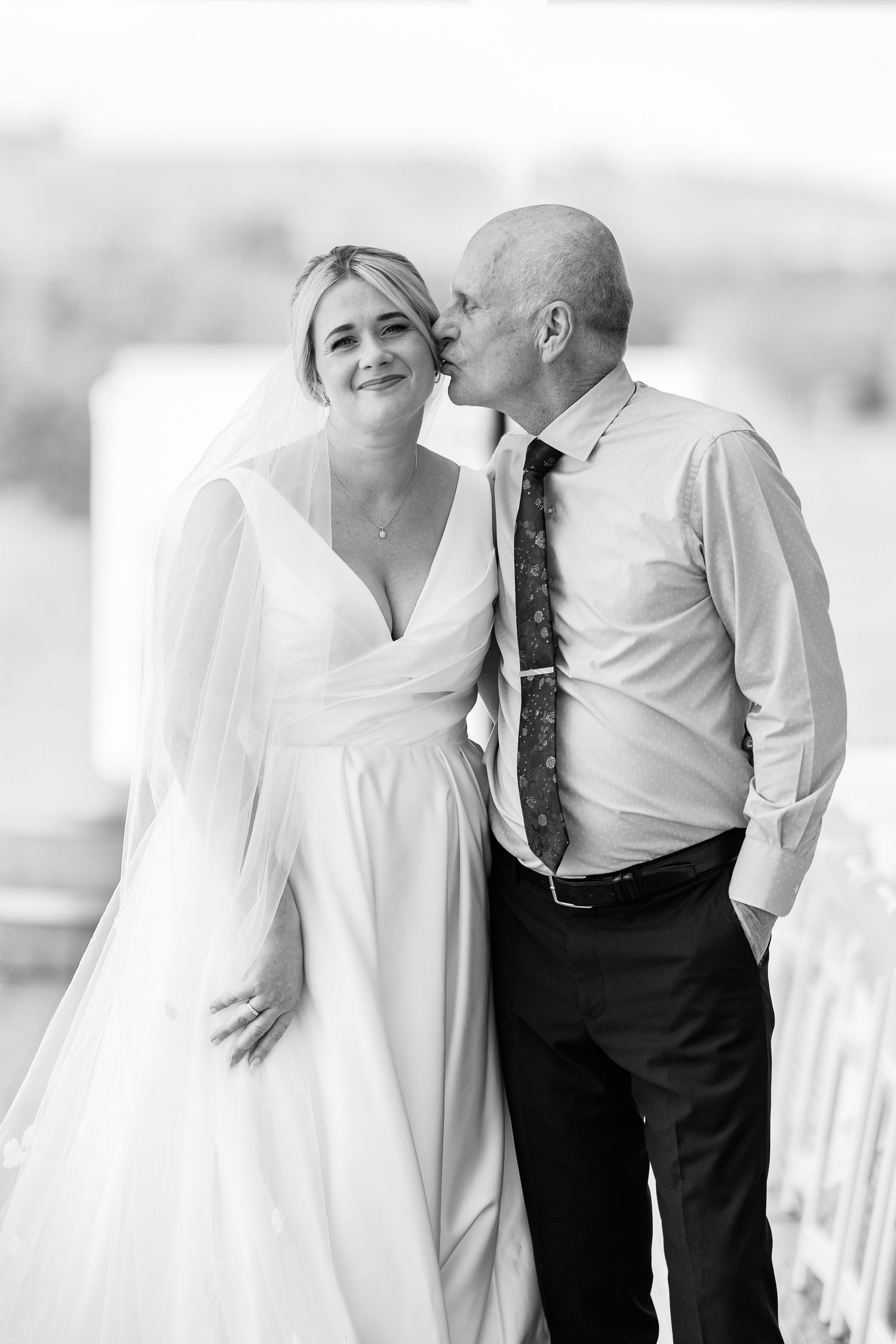 A tender wedding portrait showing a couple in white dress and formal attire against a bright background.