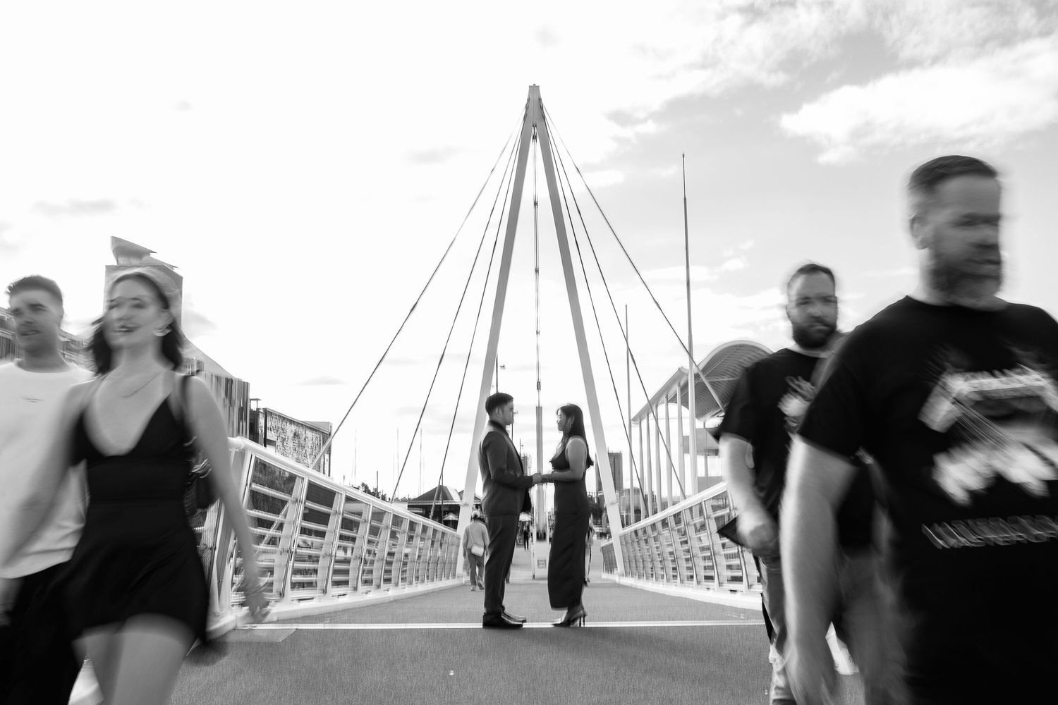 Bridge walkway with motion blur of pedestrians crossing against bright sky.