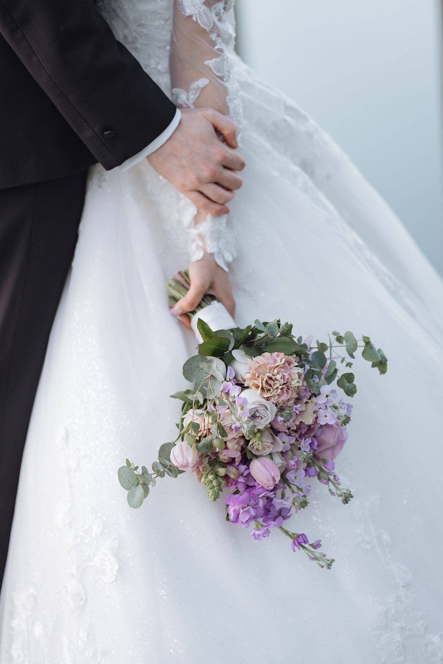 Elegant bridal bouquet with purple flowers and eucalyptus leaves against a white wedding dress.