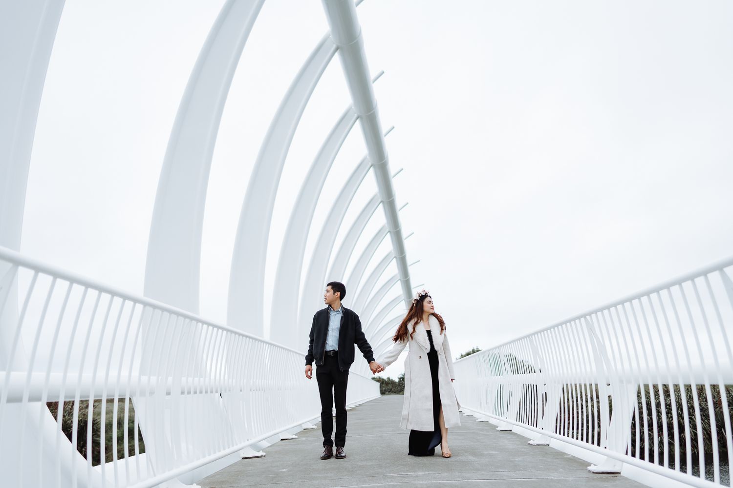 Couple walking through a modern white architectural tunnel with curved walls and natural lighting.